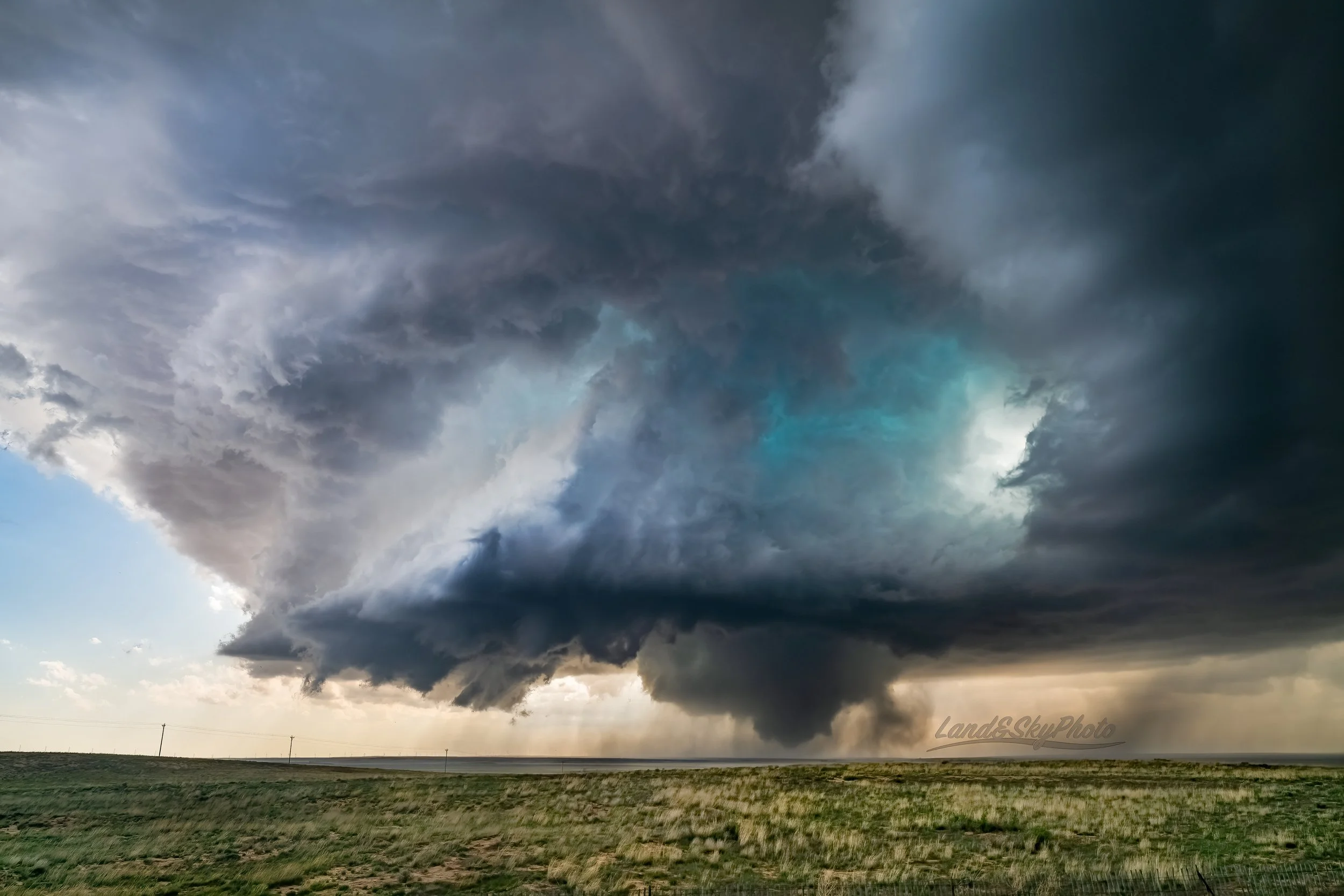 A large tornado spins in open New Mexico ranch land with its gorgeous parent supercell above.