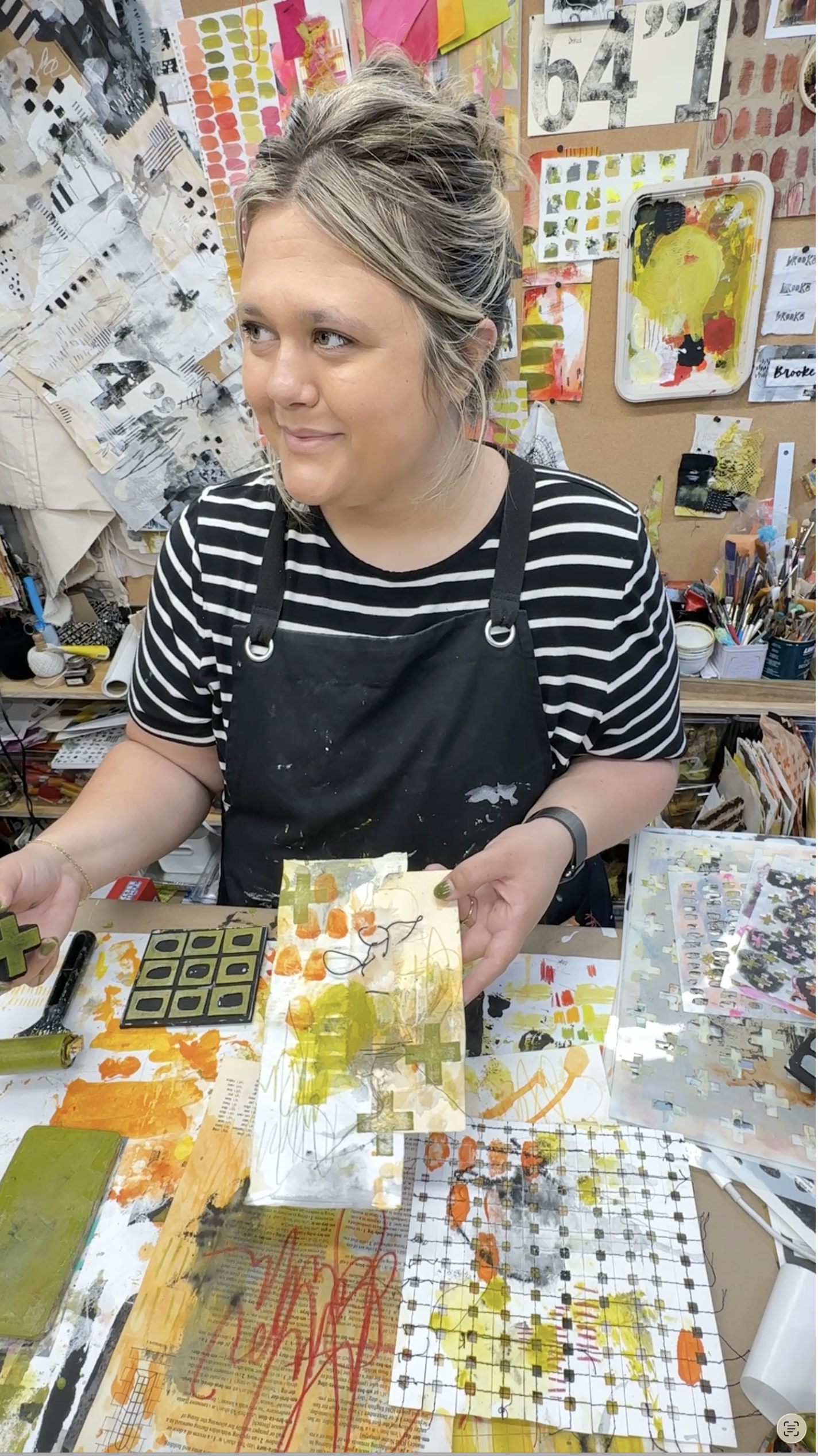 BB Henry smiling + creating art in studio, bright and colorful bulletin board in background