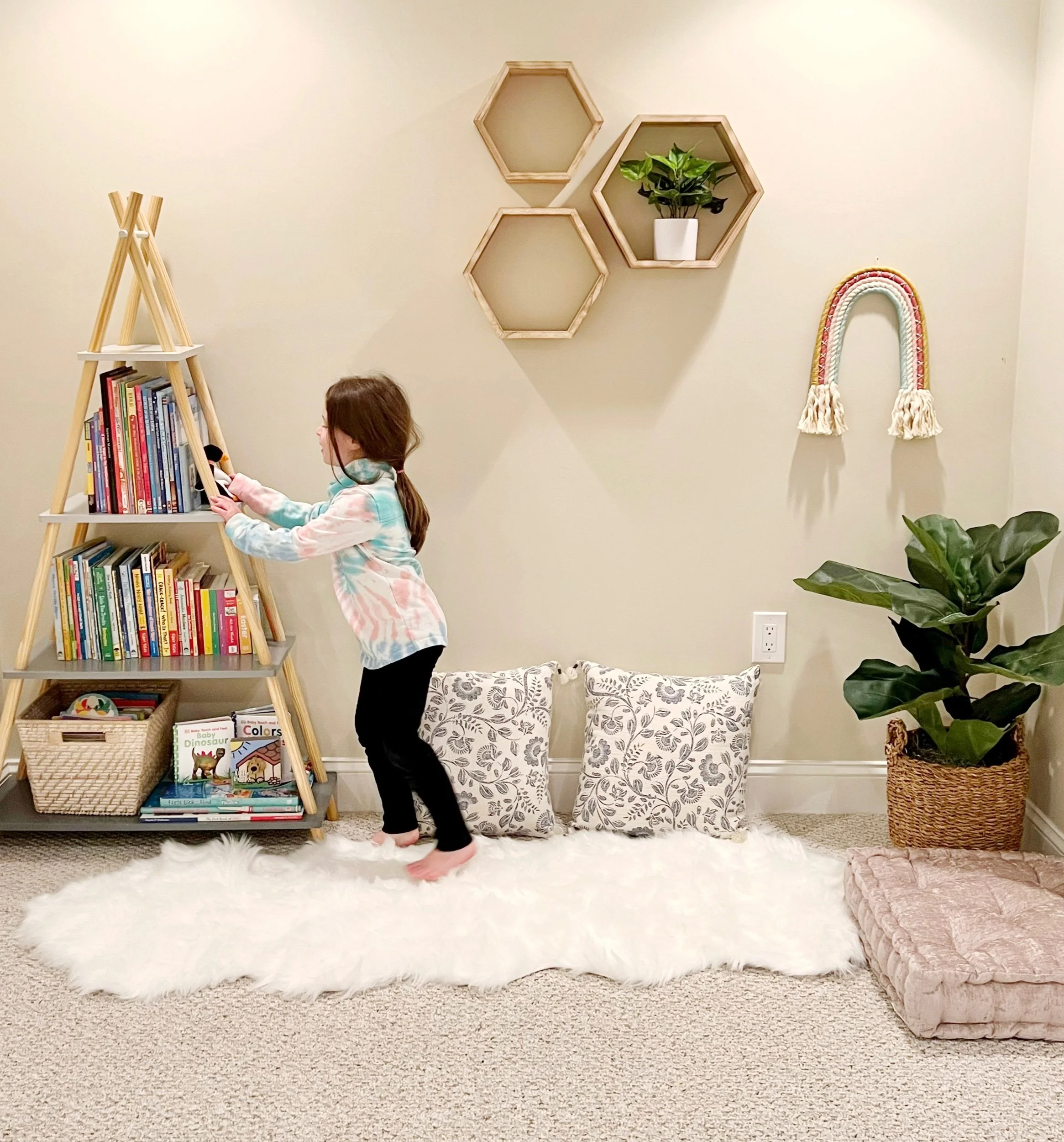 Child's basement playroom with teepee bookshelf, floating decorative shelves, and cozy corner with large plant