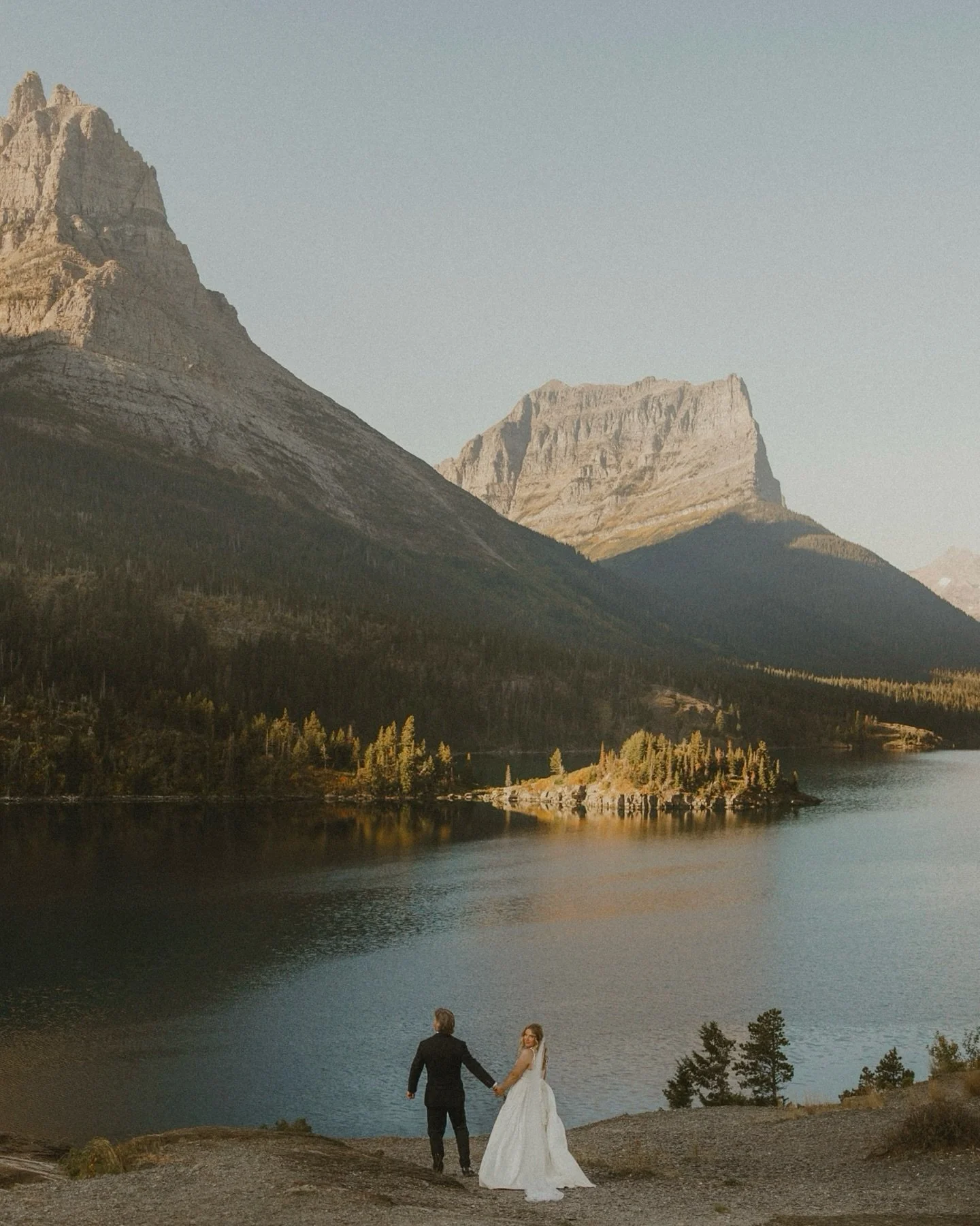Erin and Wade at Sun Point, about an hour after sunrise, where they shared vows in Montana. Wrapped in the softest light and framed by giants, the valley held onto dawn well into the morning. The ethereal glow rippled across Saint Mary Lake, while th