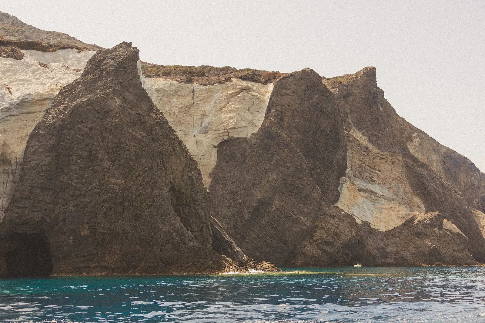 Cliffs with large rock formations along the shoreline, with water in the foreground and a small boat near the rocks.