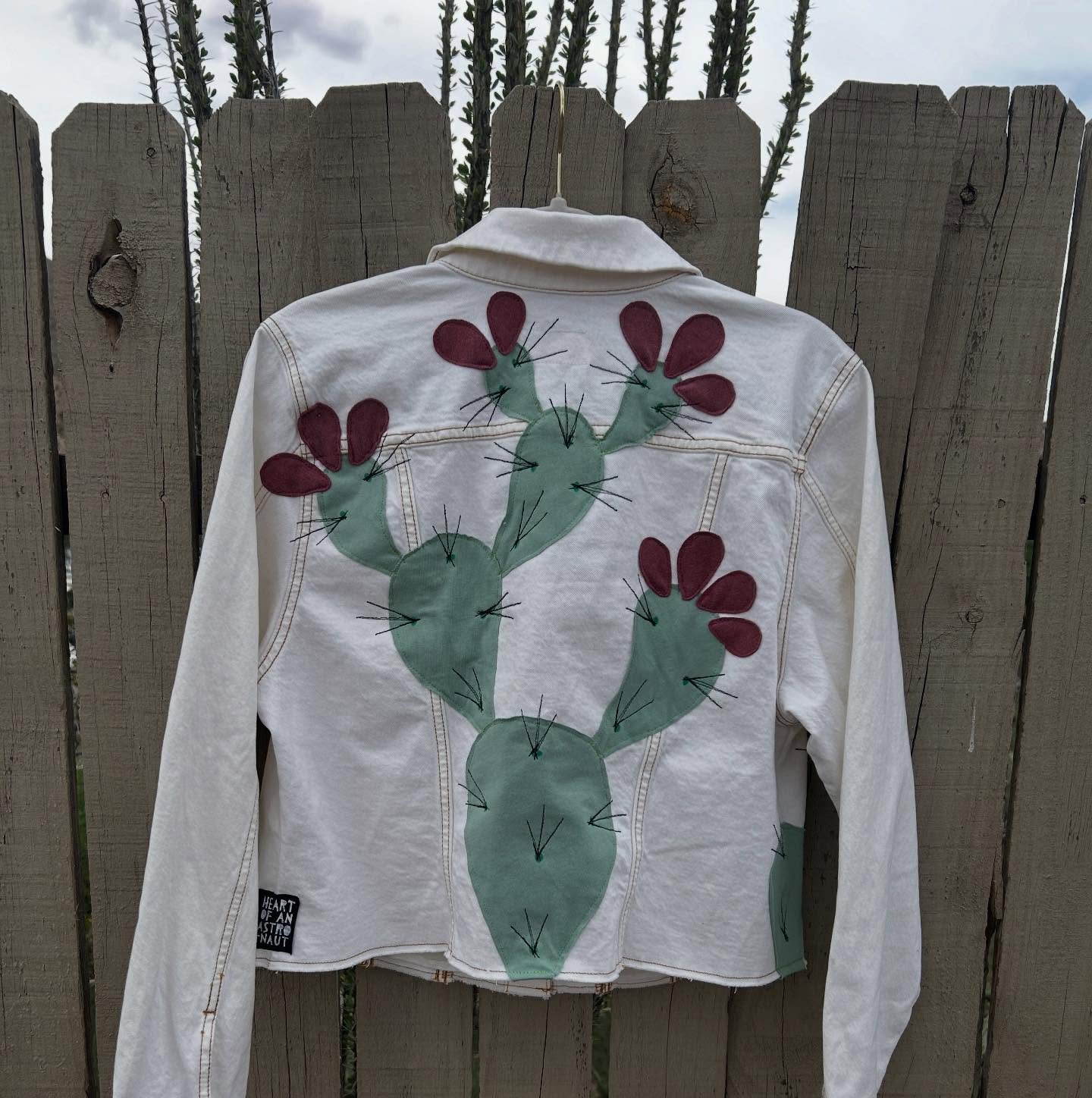 White Universal Thread denim jacket with gold buttons and dusty rose prickly pears in back and front, paired with hand drawn fabric dye Zia on left breast. $129 measurements are in the listing on my website, link in bio. #upcyclefashion #pricklypears