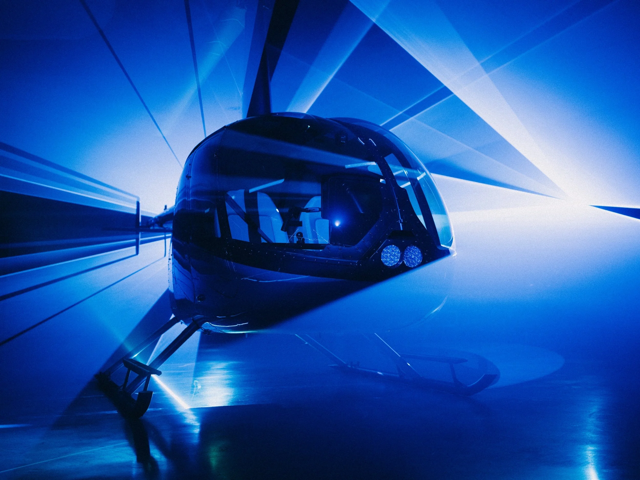 A helicopter illuminated in blue light, viewed through a glass surface with light beams creating a dynamic background.