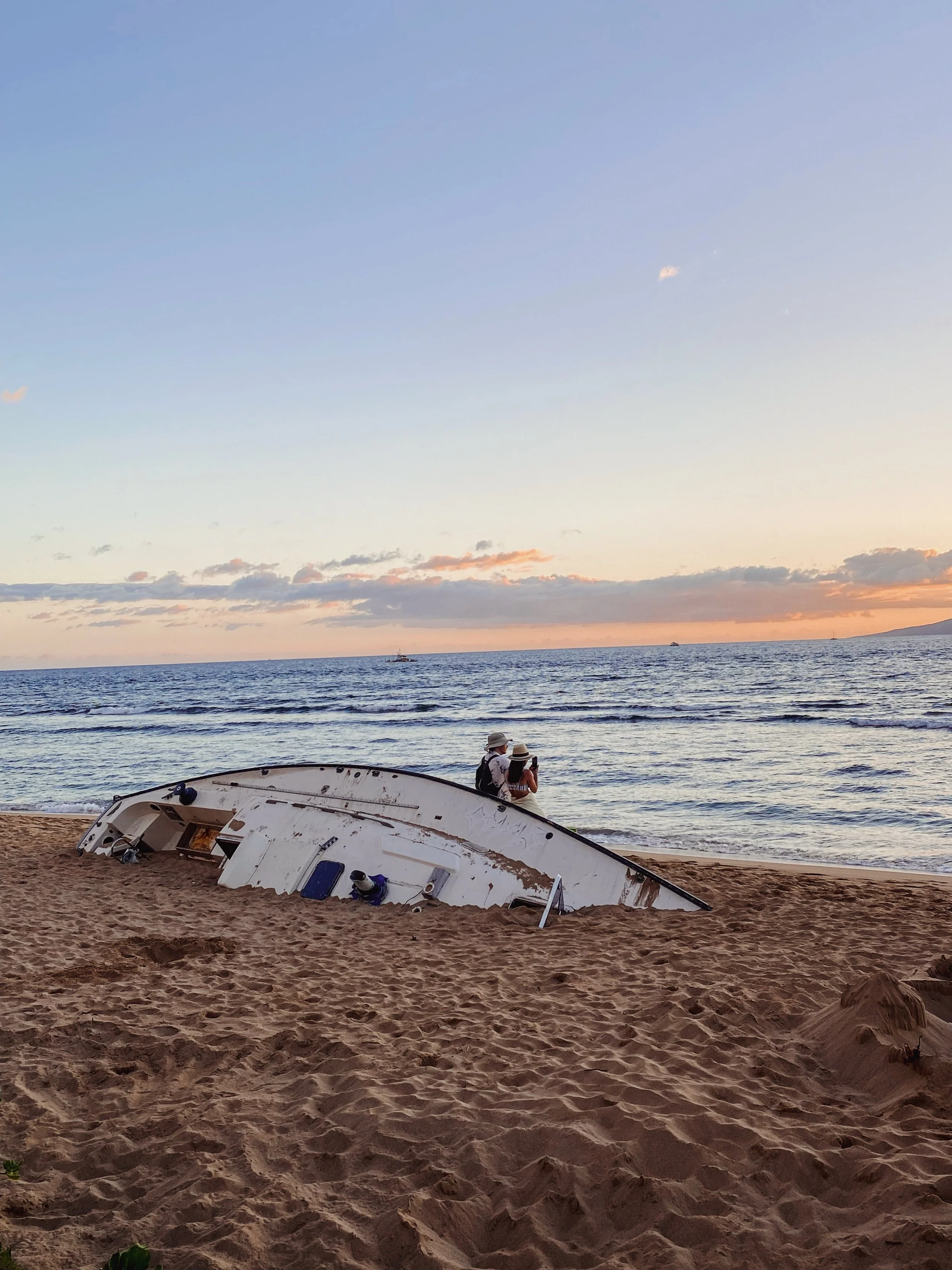 Two lovers sitting on the edge of a washed up boat on a Hawaiian beach at sunset. 