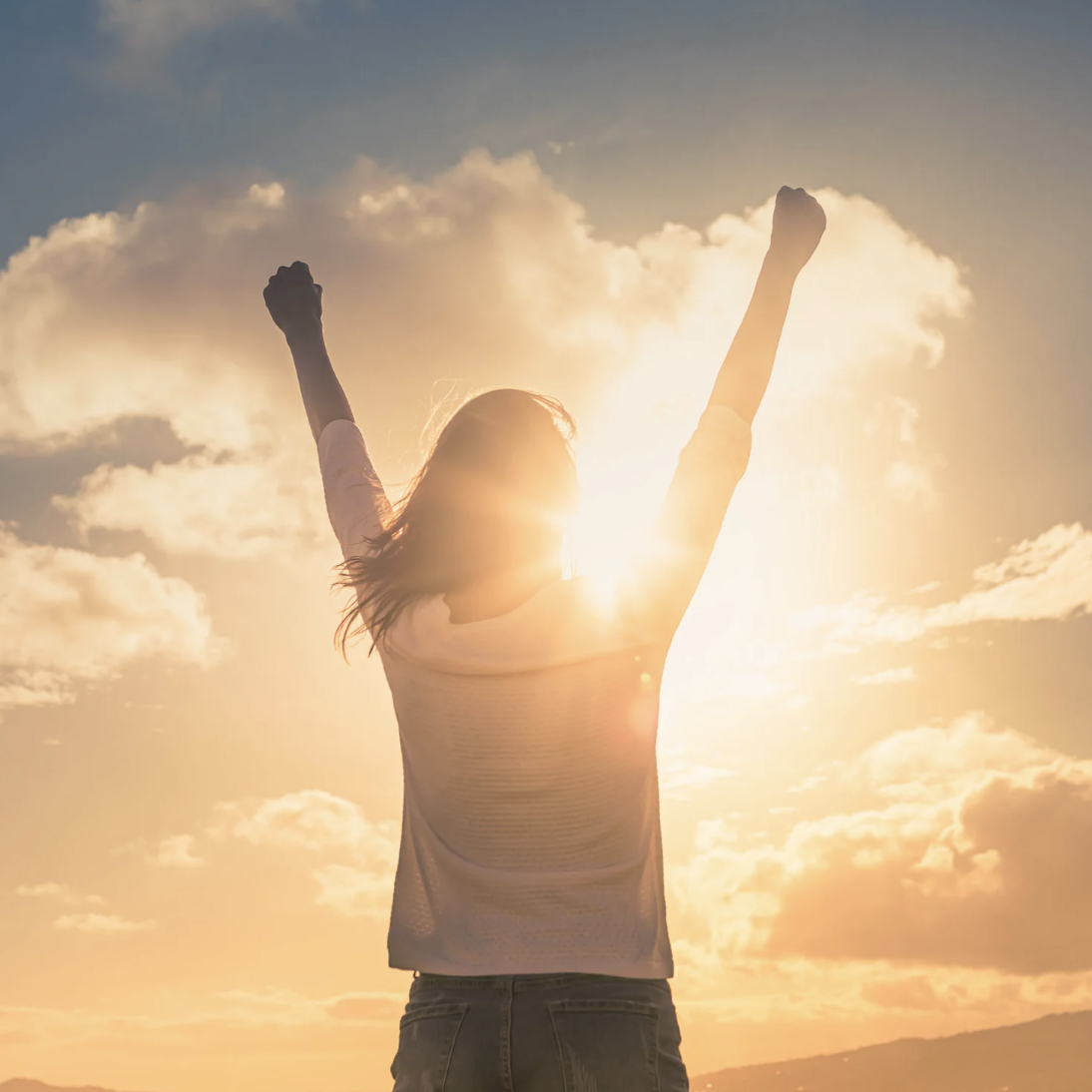 Woman raising her arms triumphantly under the gentle glow of the sun