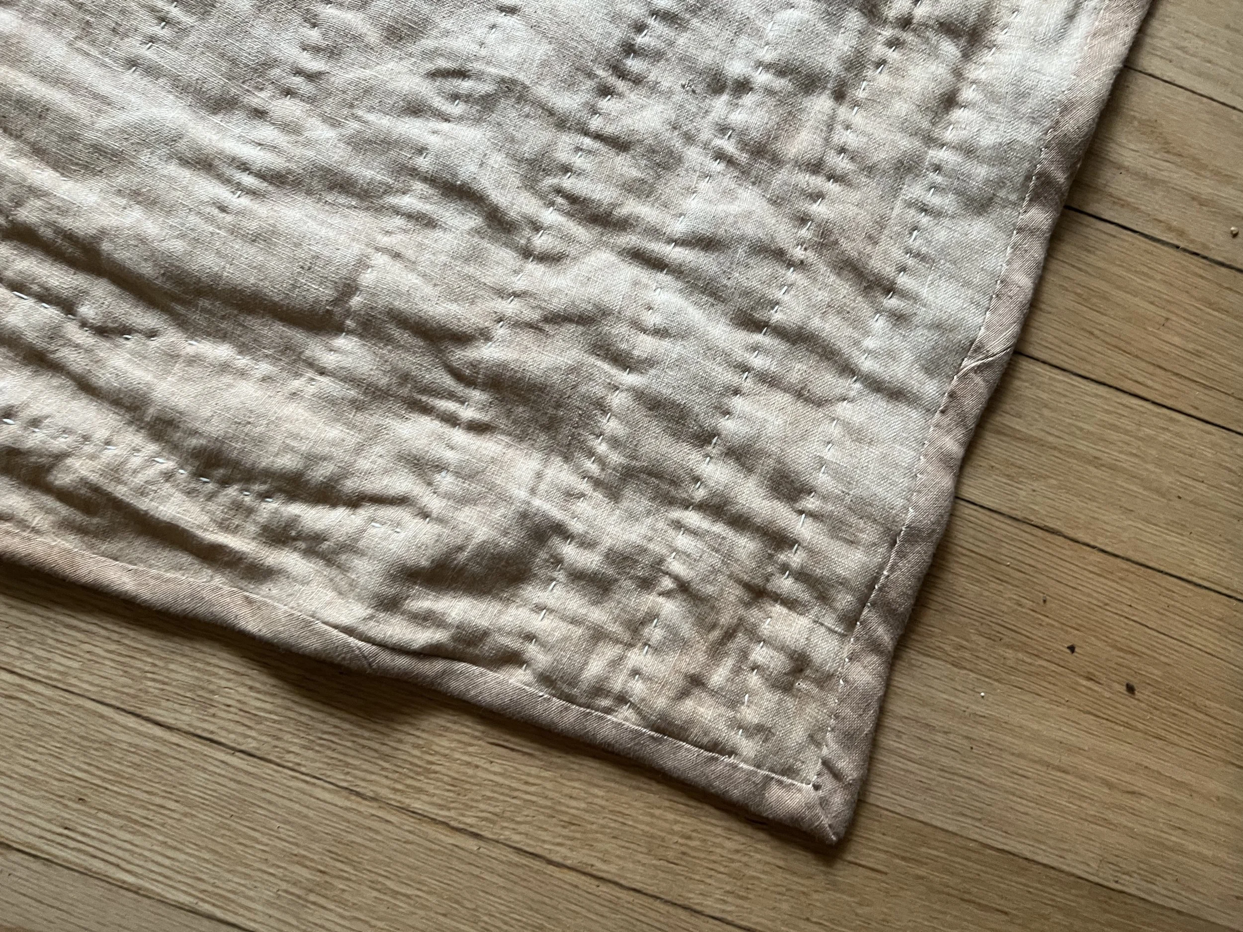 Corner of a beige quilted fabric on a wooden floor