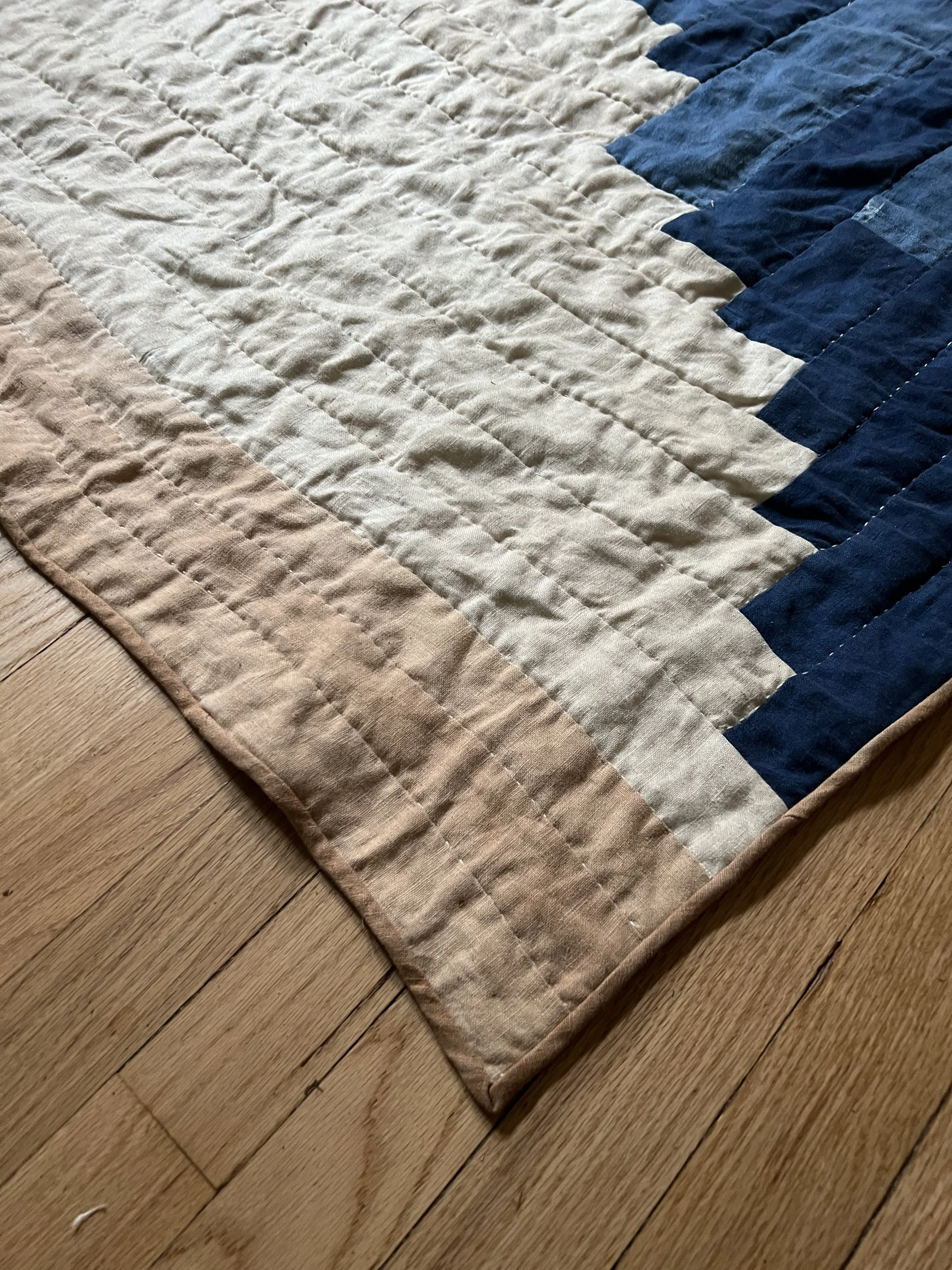 Close-up of a quilt with beige and navy blue color blocks on a wooden floor.