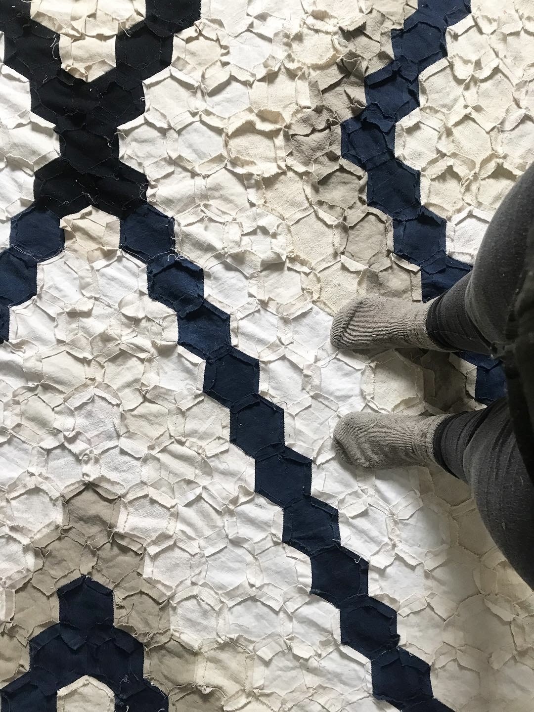 Person standing on a textured rug featuring a geometric pattern with hexagonal shapes in black and white.