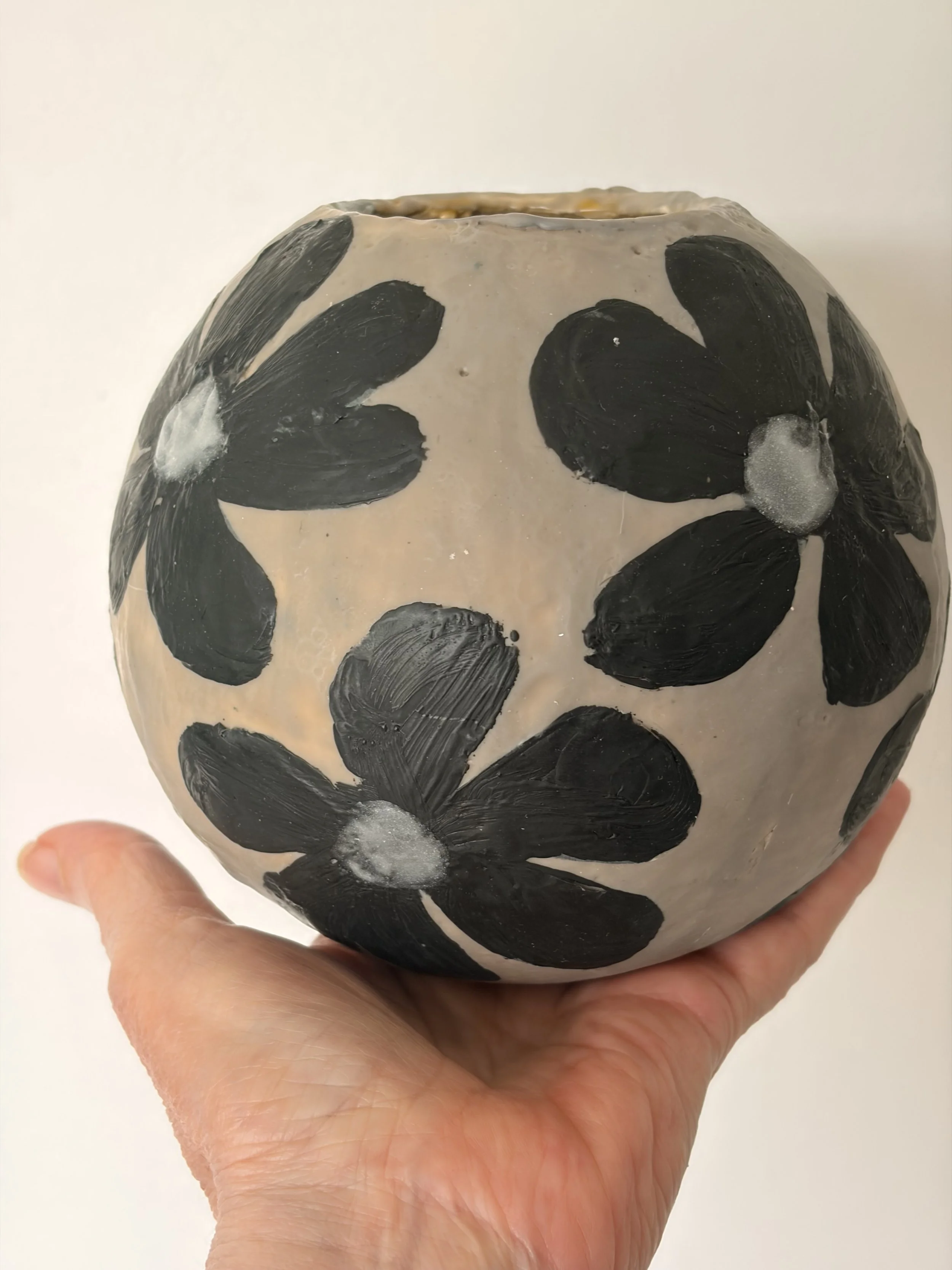 Small round encaustic wax artwork featuring dark floral forms and textured layers in black and earthy tones, titled Black Daisies.