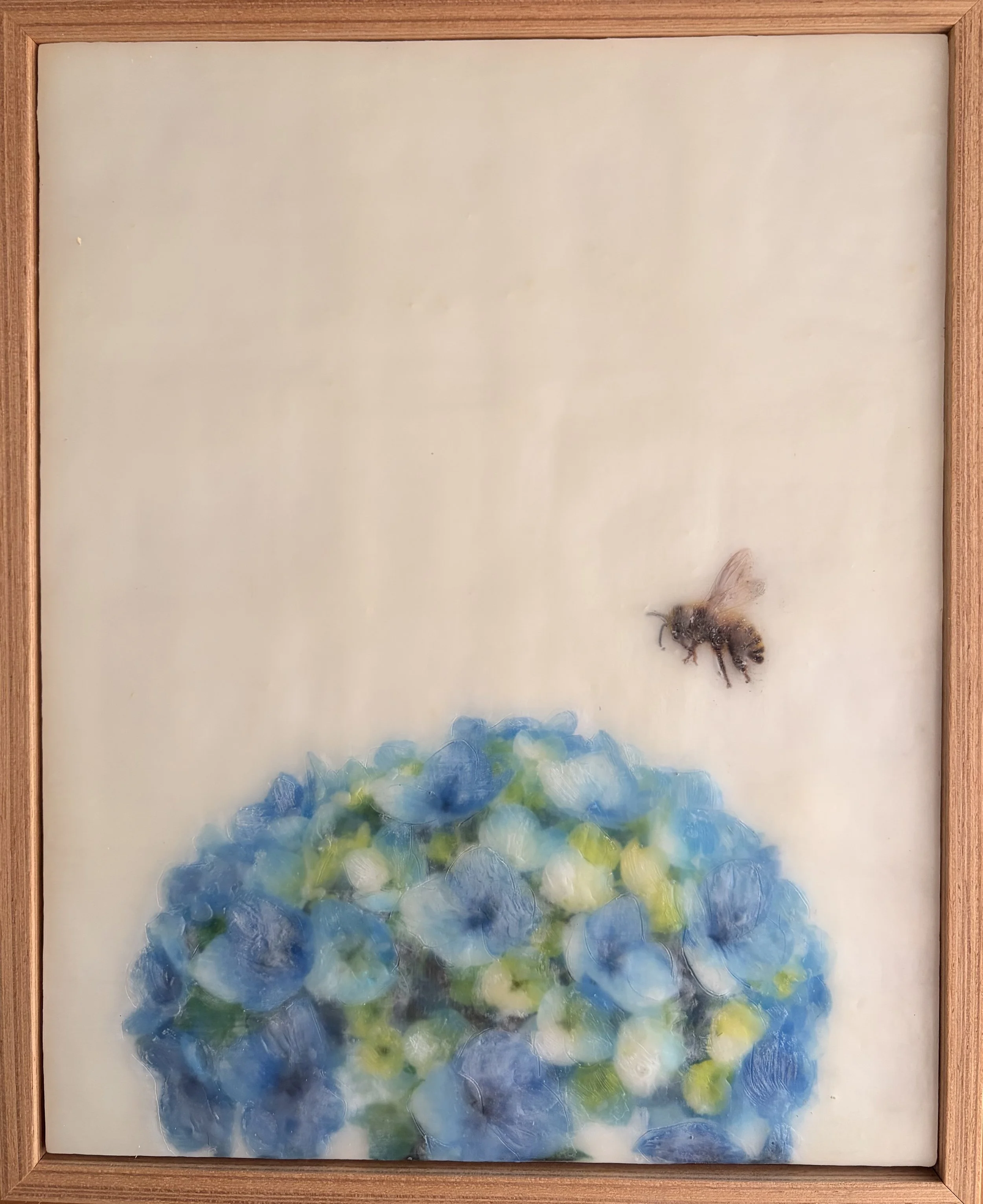 Original encaustic wax artwork featuring a honeybee hovering above blue hydrangea flowers, framed in Tasmanian oak with soft translucent beeswax layers.