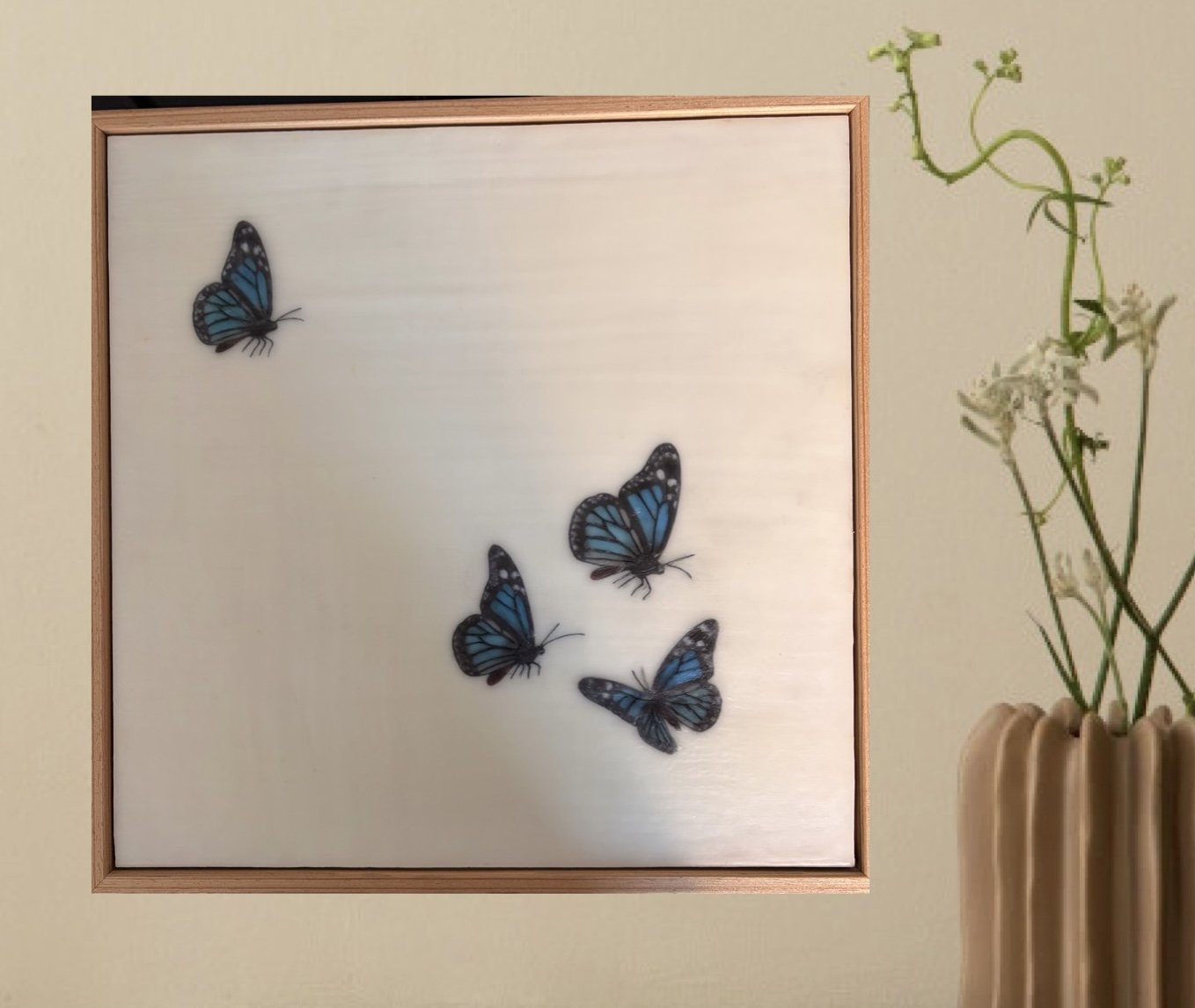 Minimalist encaustic wax artwork featuring four blue butterflies floating across a luminous ivory background within a natural timber frame. Contemporary, serene wall art by Karen Canning.