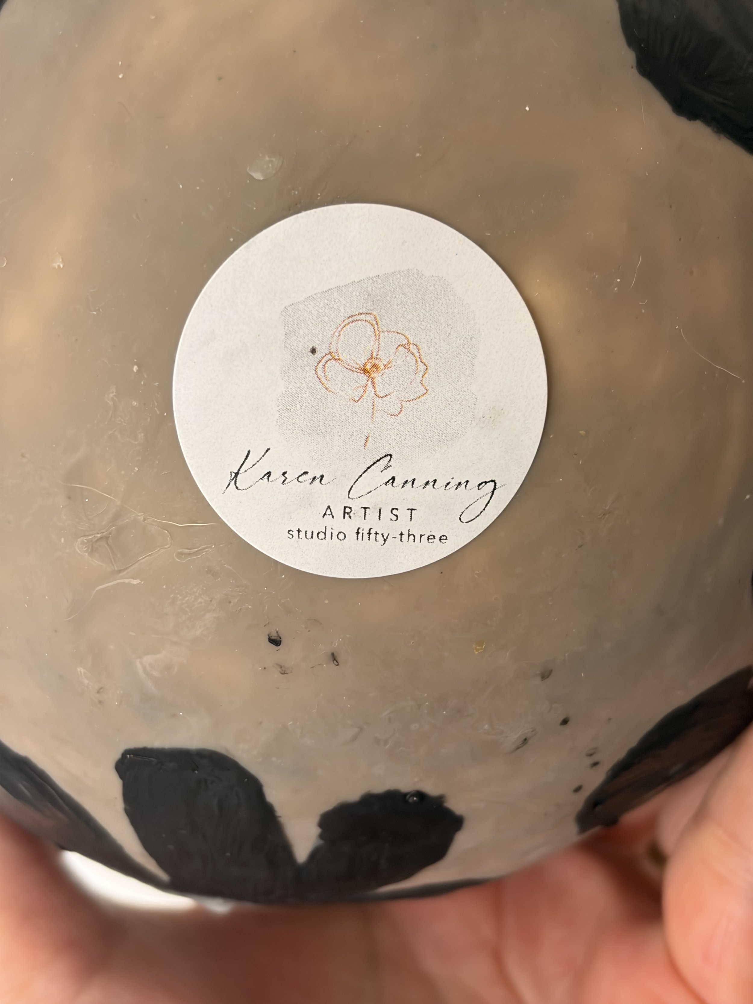 Small round encaustic wax artwork featuring dark floral forms and textured layers in black and earthy tones, titled Black Daisies.