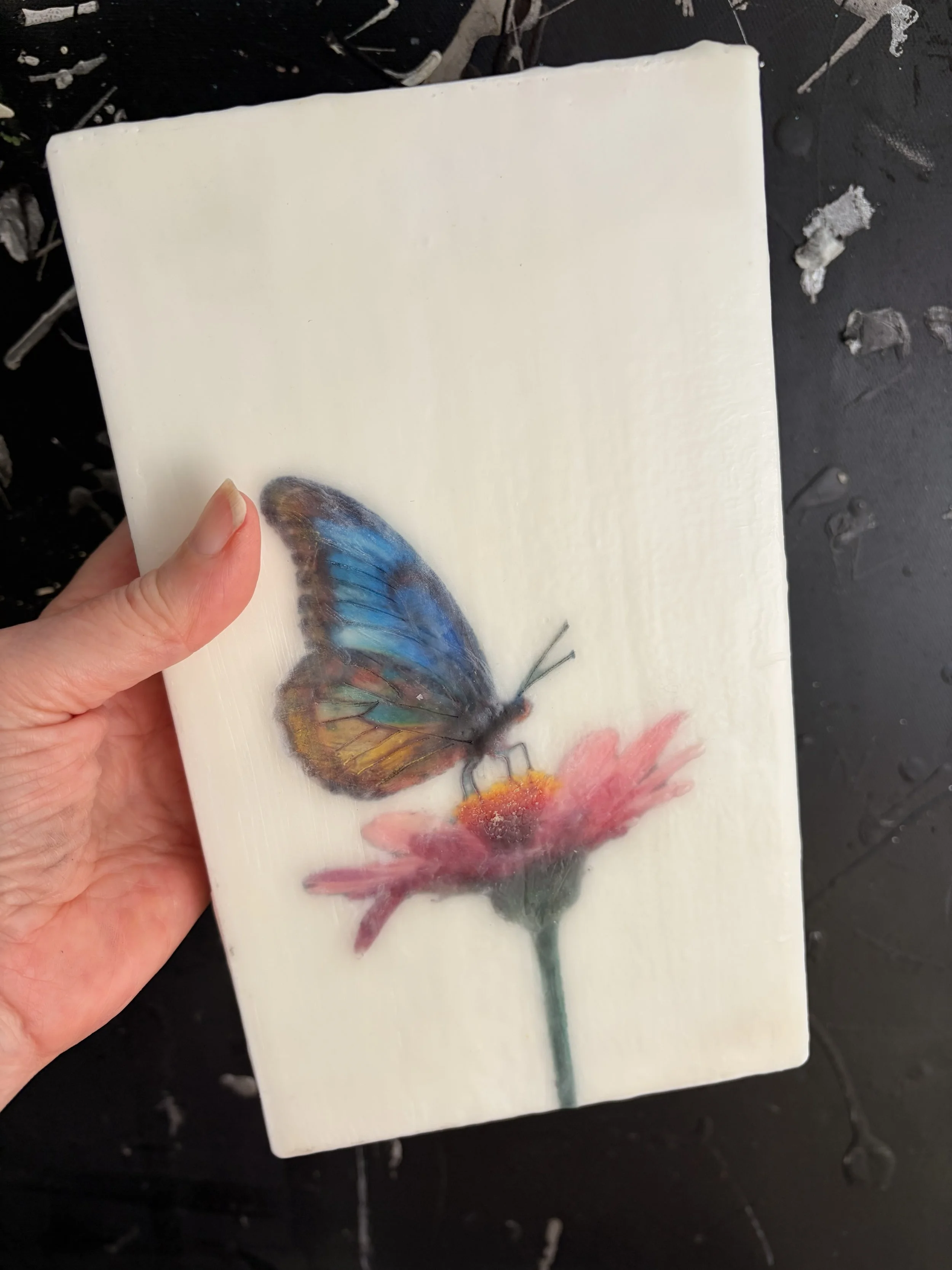 A blue and gold butterfly resting on a pink flower, rendered in luminous encaustic wax and mixed media with a dreamy, ethereal finish.
