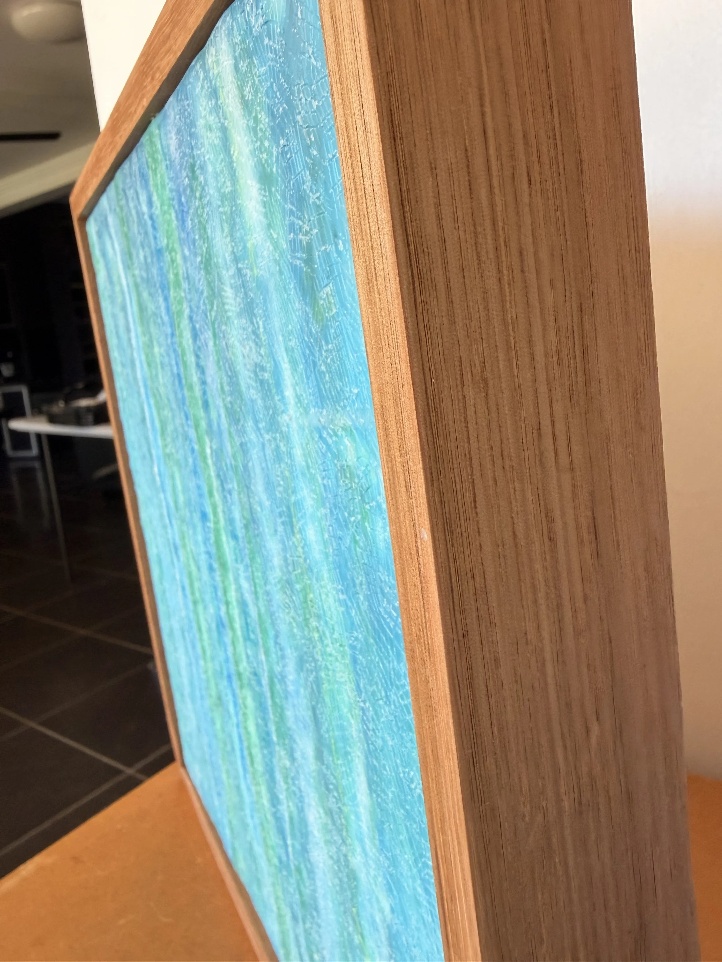 “A square 30 x 30cm encaustic wax and mixed media artwork featuring layered blue and green abstract textures, framed in natural timber.”