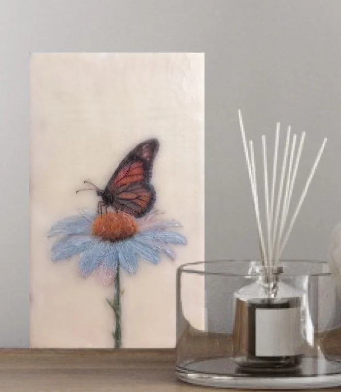 A warm orange butterfly perched on a pale blue daisy, created with encaustic wax and mixed media, featuring rich texture and soft botanical details.