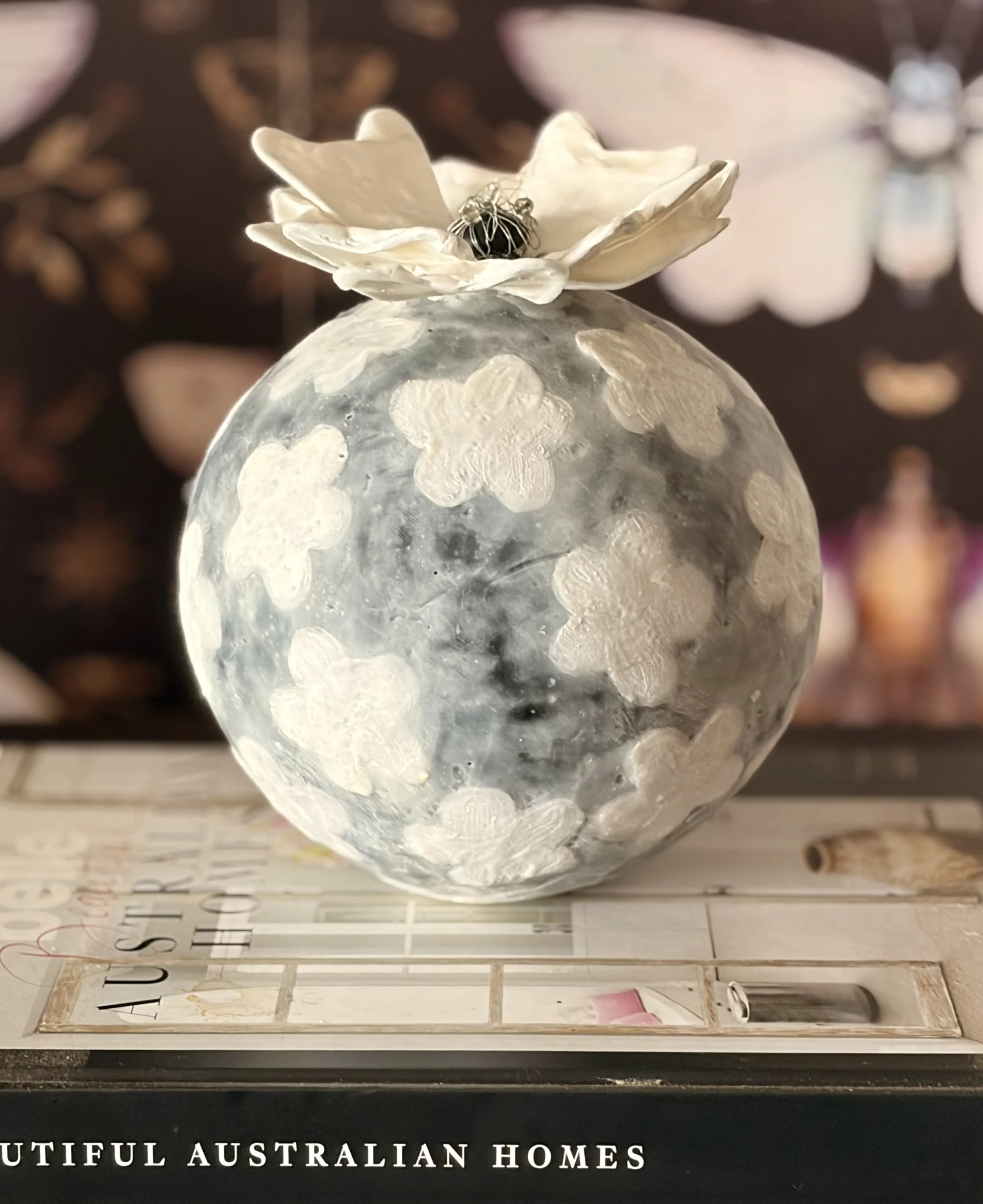 Encaustic wax and mixed media sculpture featuring a round grey textured form with raised white floral patterns and a sculptural white flower on top, displayed as a decorative art object.