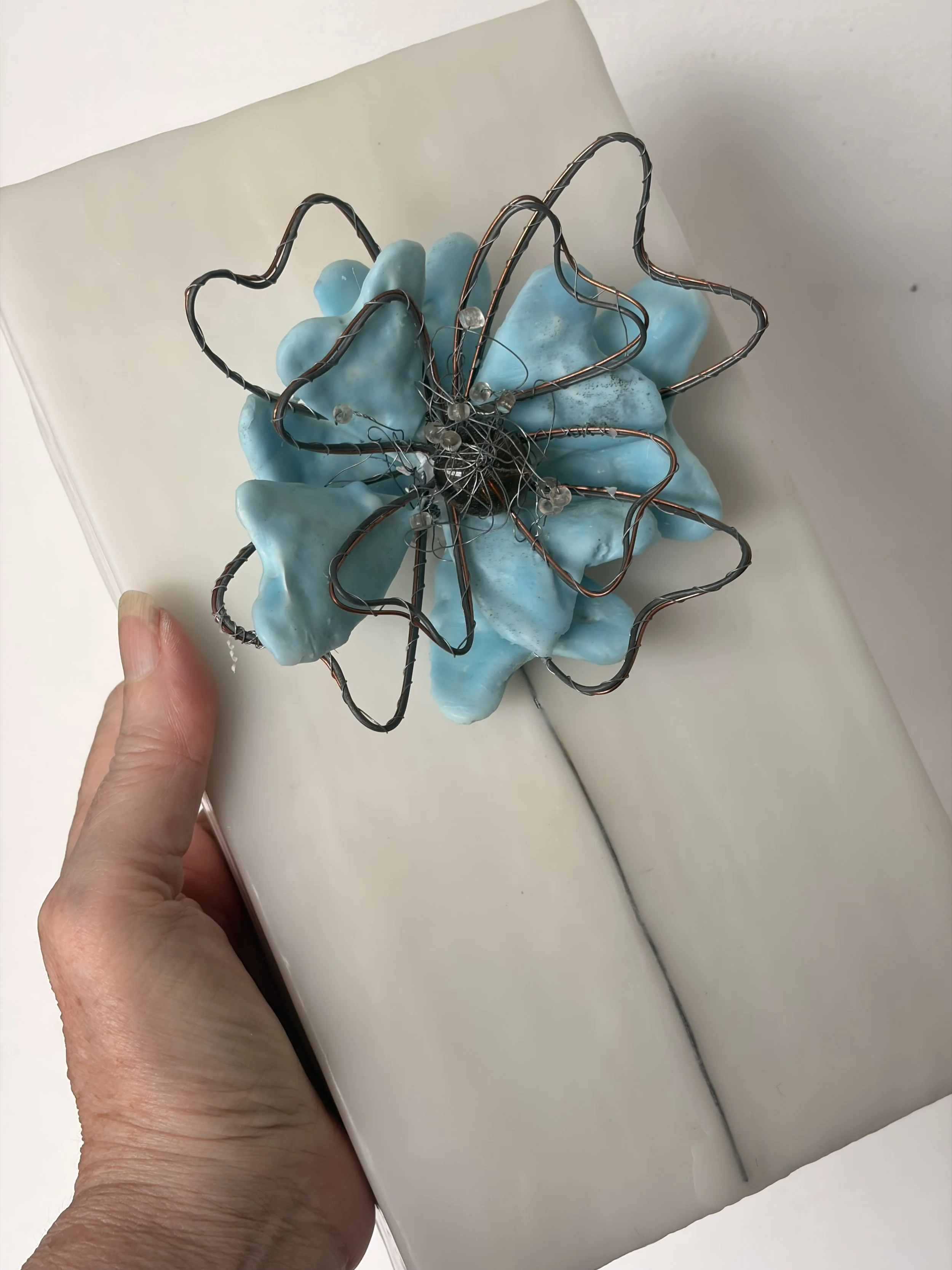 Close-up of hand-shaped wire details over blue encaustic wax petals