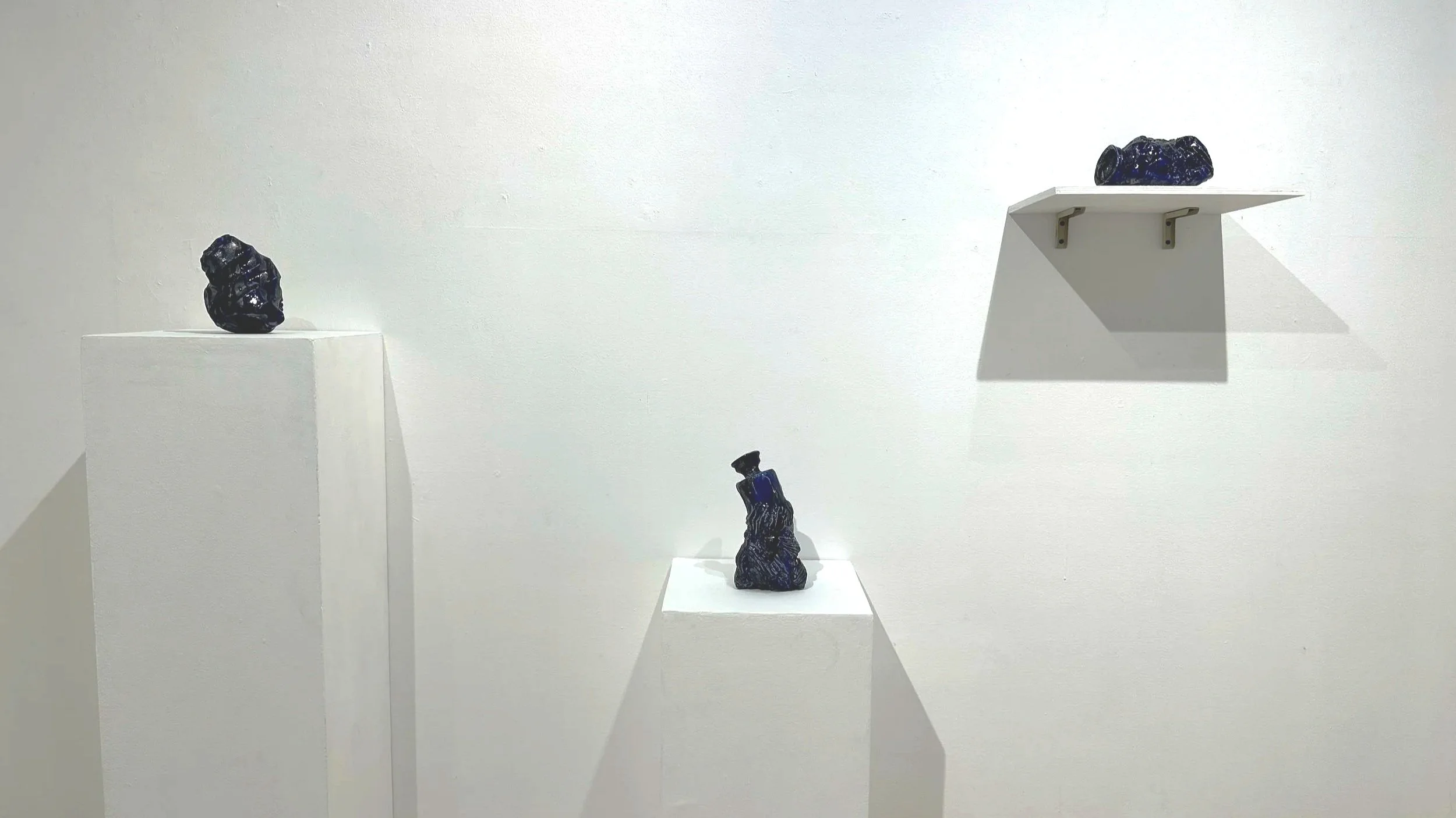 Three dark ceramic sculptures by Jose Solon Perfecto on white pedestals