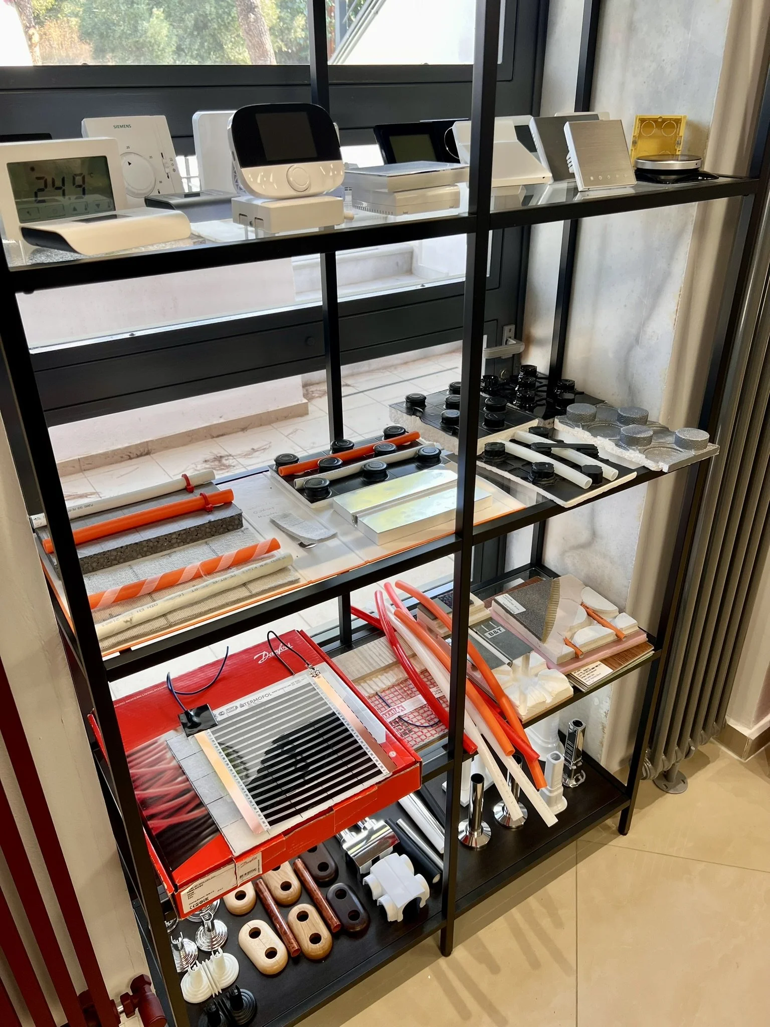 Underfloor heating material samples such as pipes, insulation, and thermostats at Tsolakidis store display
