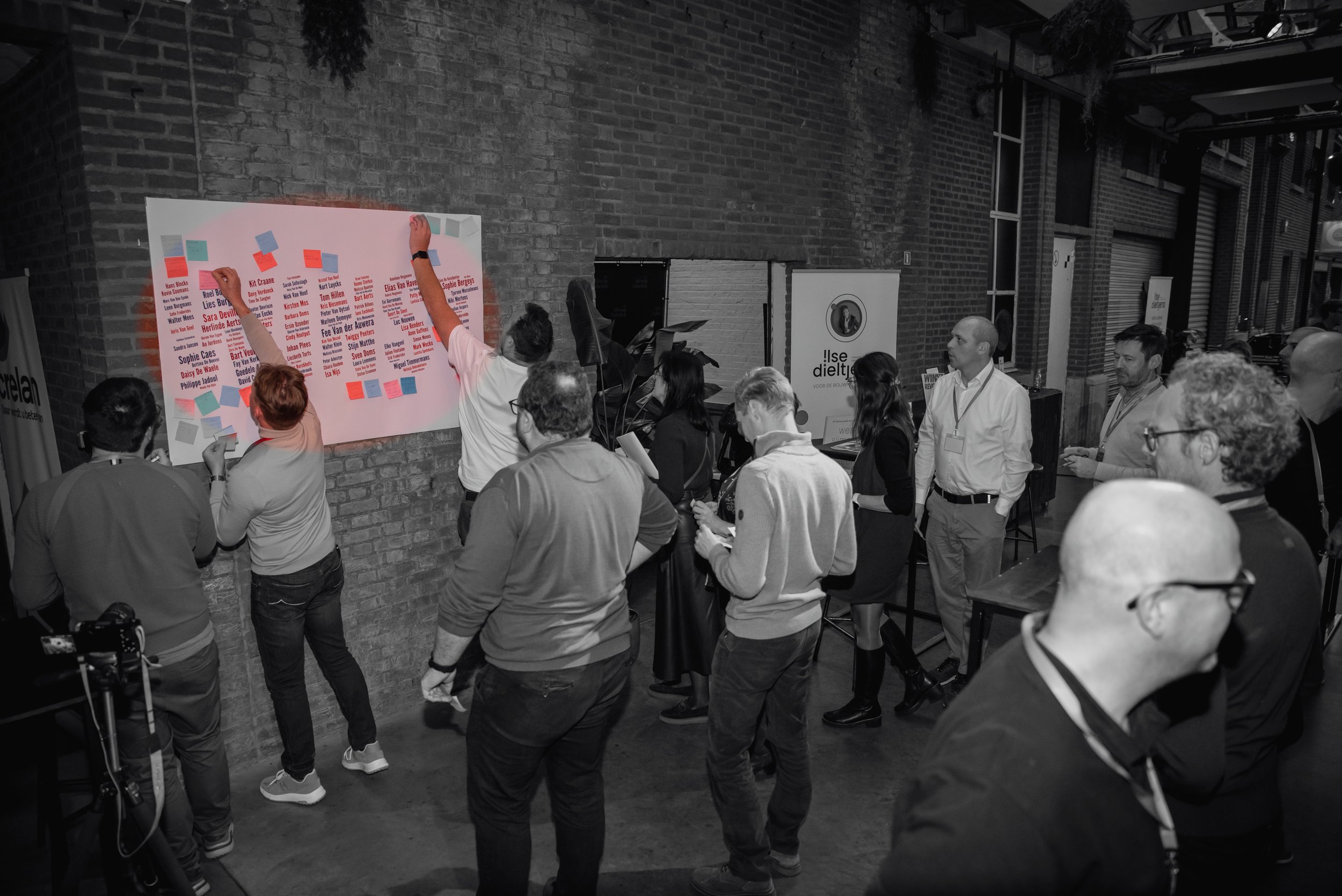 Mensen die op een conferentie of vergadering een diagram of plan op een muur vastmaken, binnen een ruimte met bakstenen muren.