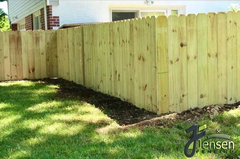 Newly built wooden privacy fence in backyard with green grass and partially visible house in background.