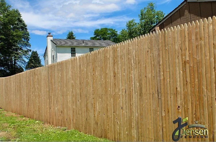 New wooden privacy fence along a yard with a house and trees in the background.