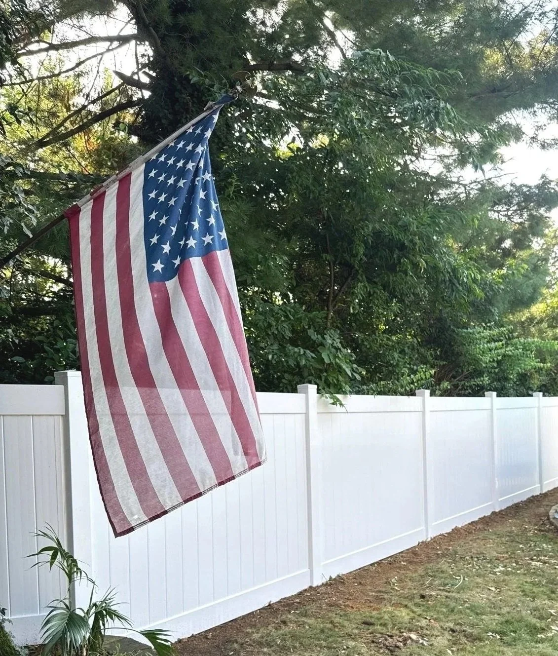 American flag hanging from a fence near trees and greenery.