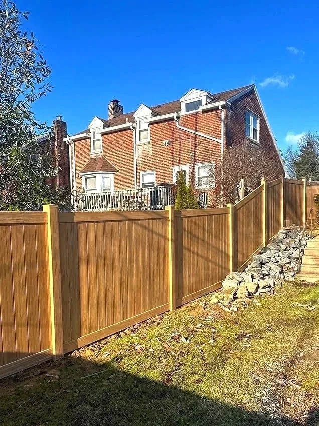 New wooden fence installed along yard with pile of rocks next to steps leading up the slope.