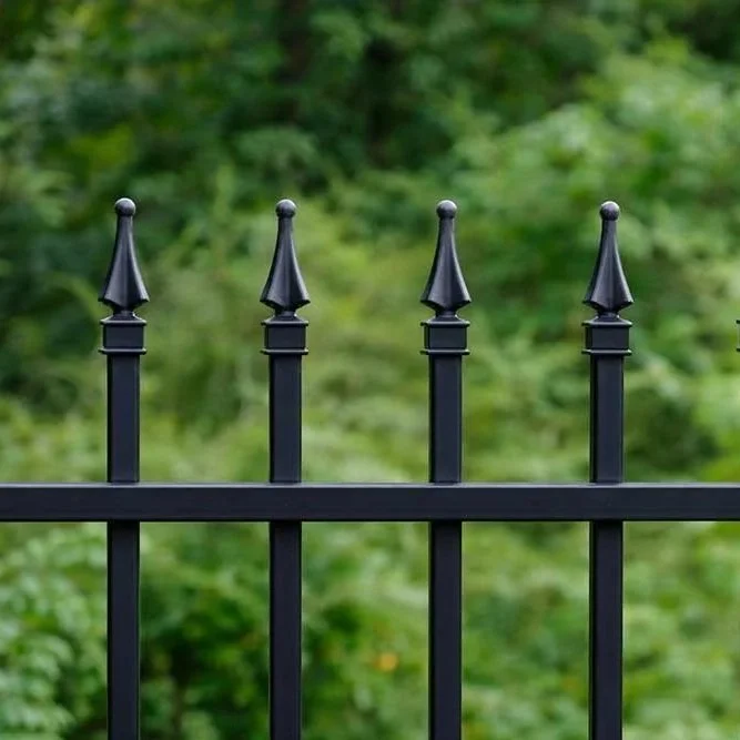Close-up of a black metal fence with pointed finials, with green trees in the background.