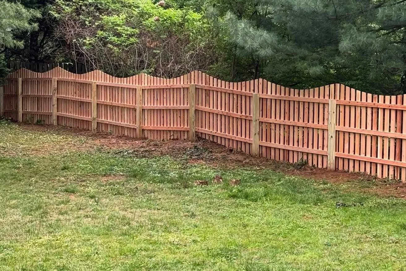 A newly installed wooden fence lining a grassy yard with trees in the background in Delaware County, PA.