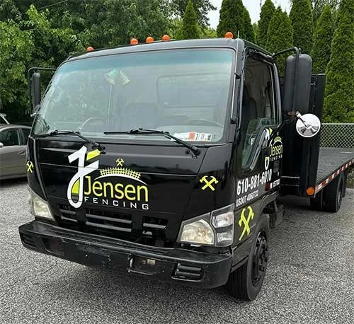 Black fencing and construction truck with Jensen Fencing logo and contact information parked on asphalt with greenery in the background.