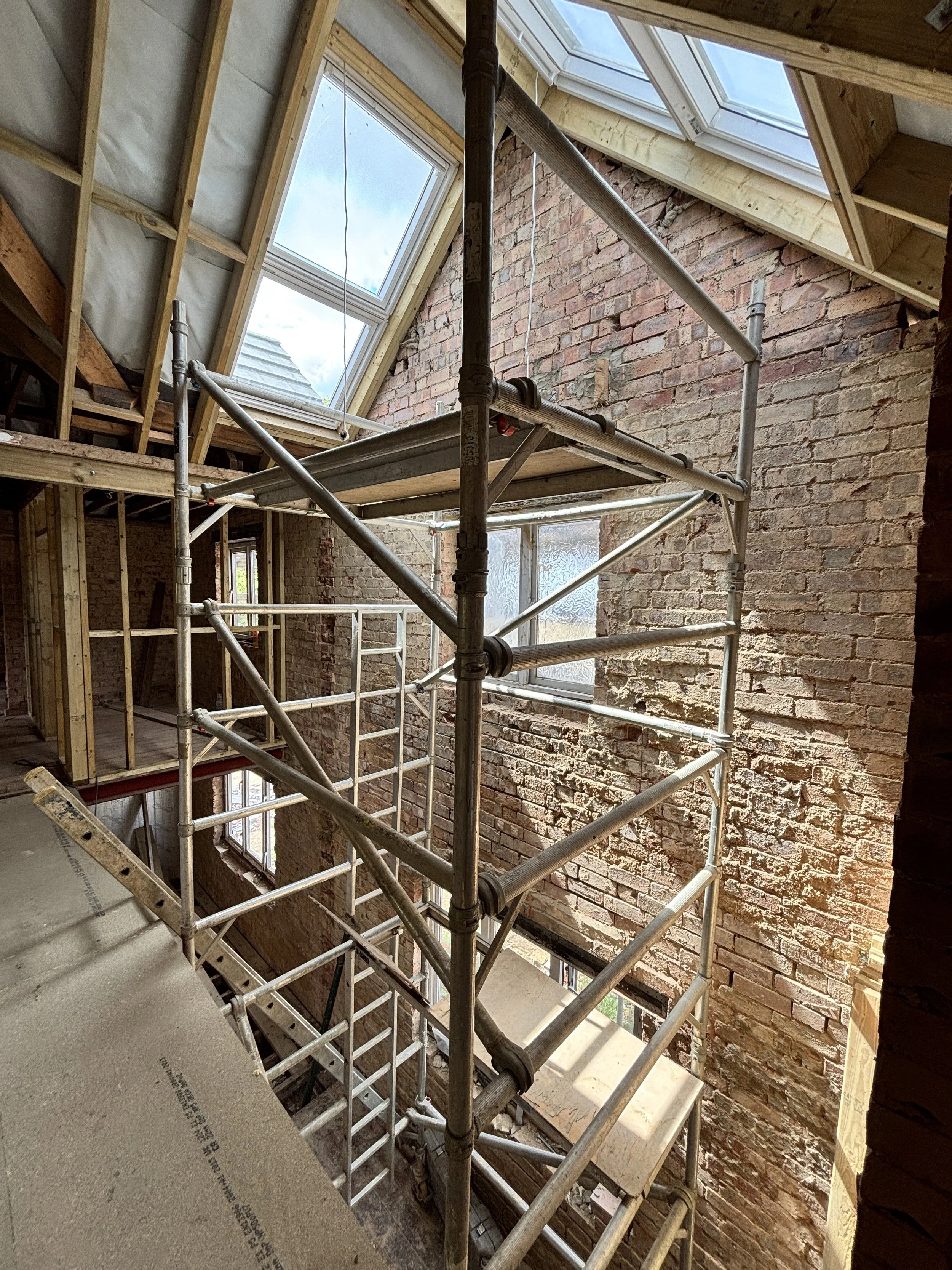 Indoor construction site with scaffolding, brick walls, and a partially installed roof with skylights.