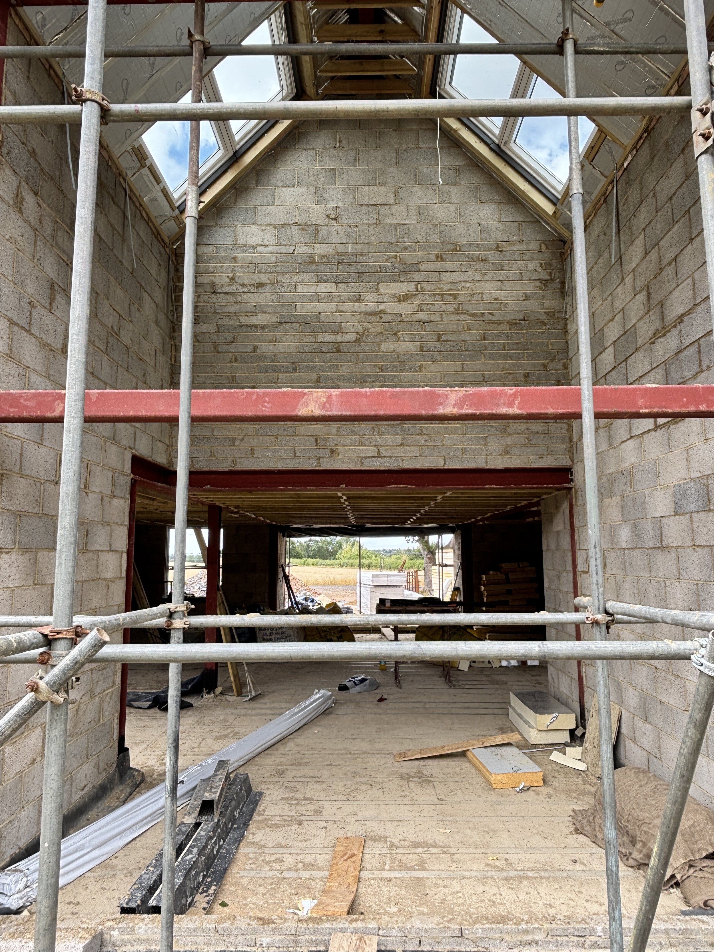 Interior view of a building under construction, with brick walls, a partially finished attic, and scaffolding inside.