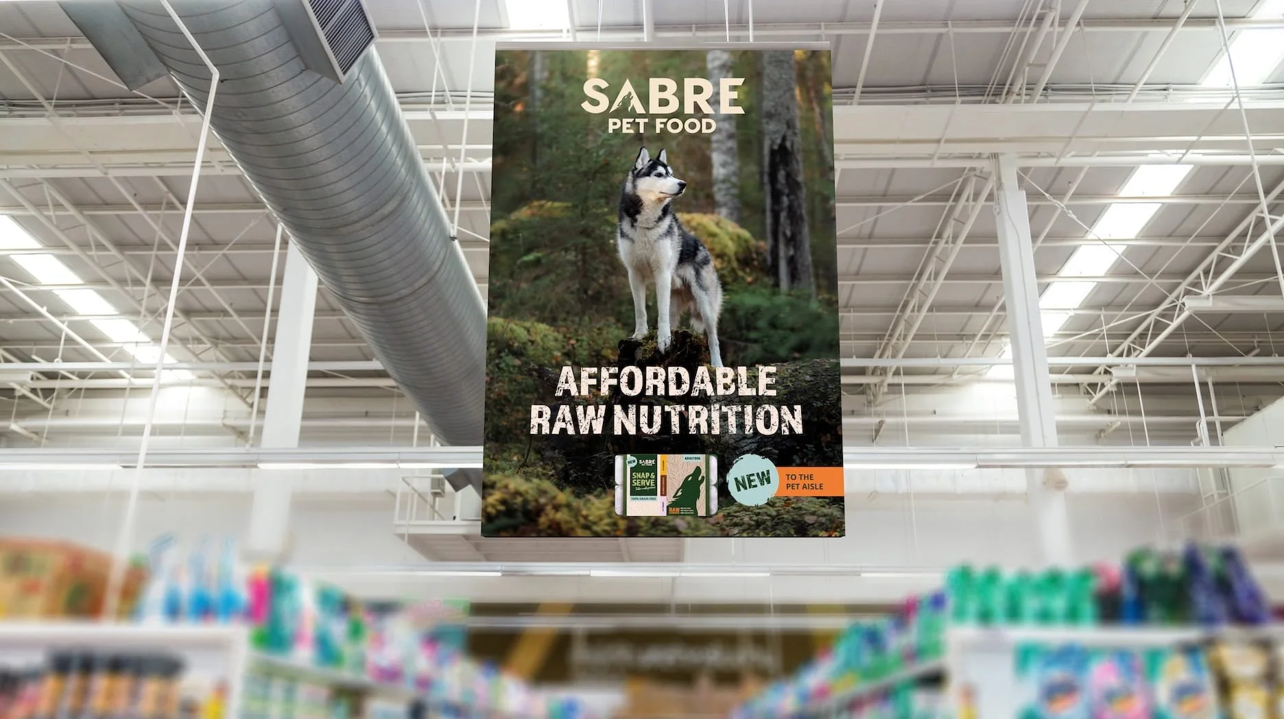 Large hanging advertisement banner in a pet store for SABRE pet food, featuring a Siberian Husky in a forest setting. The banner promotes affordable raw nutrition and mentions new products to the pet aisle. Design by Hubble.