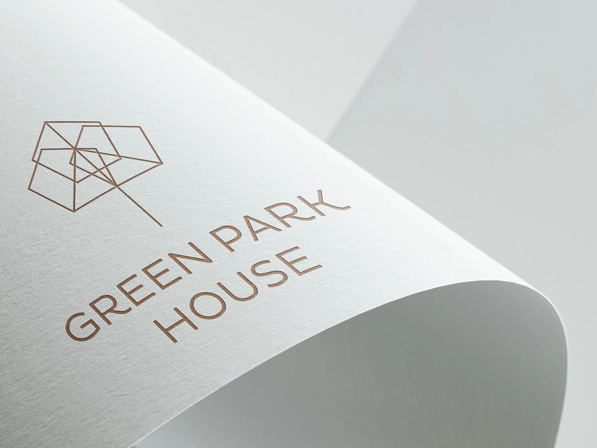 A close-up photo of a printed paper with a geometric logo and the words 'GREEN PARK HOUSE' in a copper colour on white textured paper. Design by Hubble - real estate marketing material.