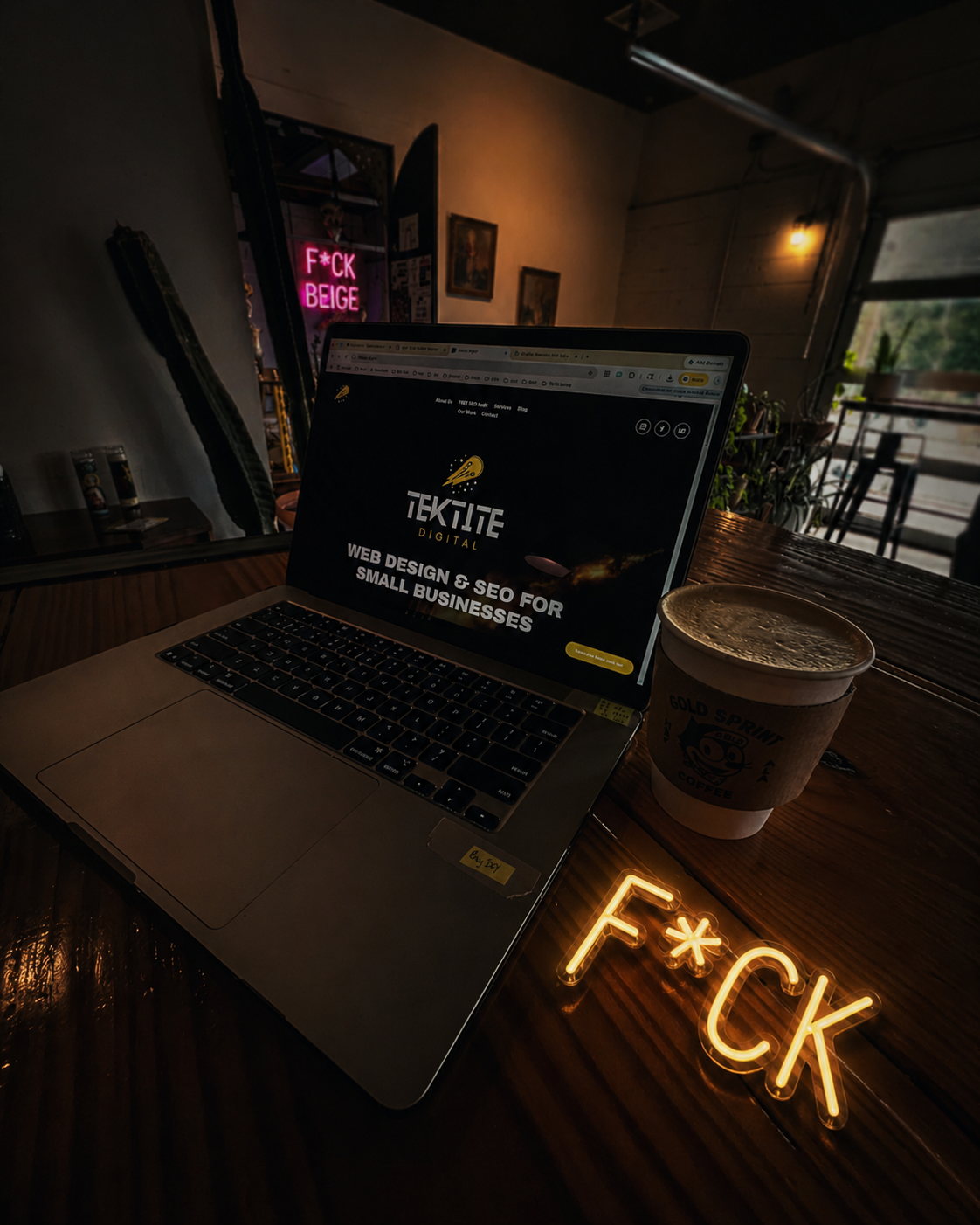 Moody coffee shop workspace with a laptop displaying the Tektite Digital website beside a coffee cup, representing modern web design, SEO, and branding for small businesses in Huntsville, Alabama.