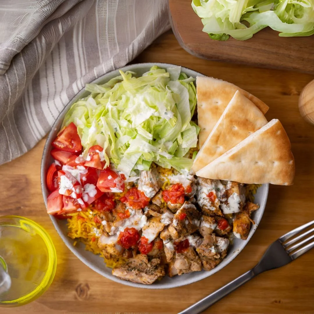 A bowl of Mexican food with shredded cheese, chopped lettuce, diced tomatoes, chicken fajitas topped with salsa, and pita bread triangles on a wooden table.