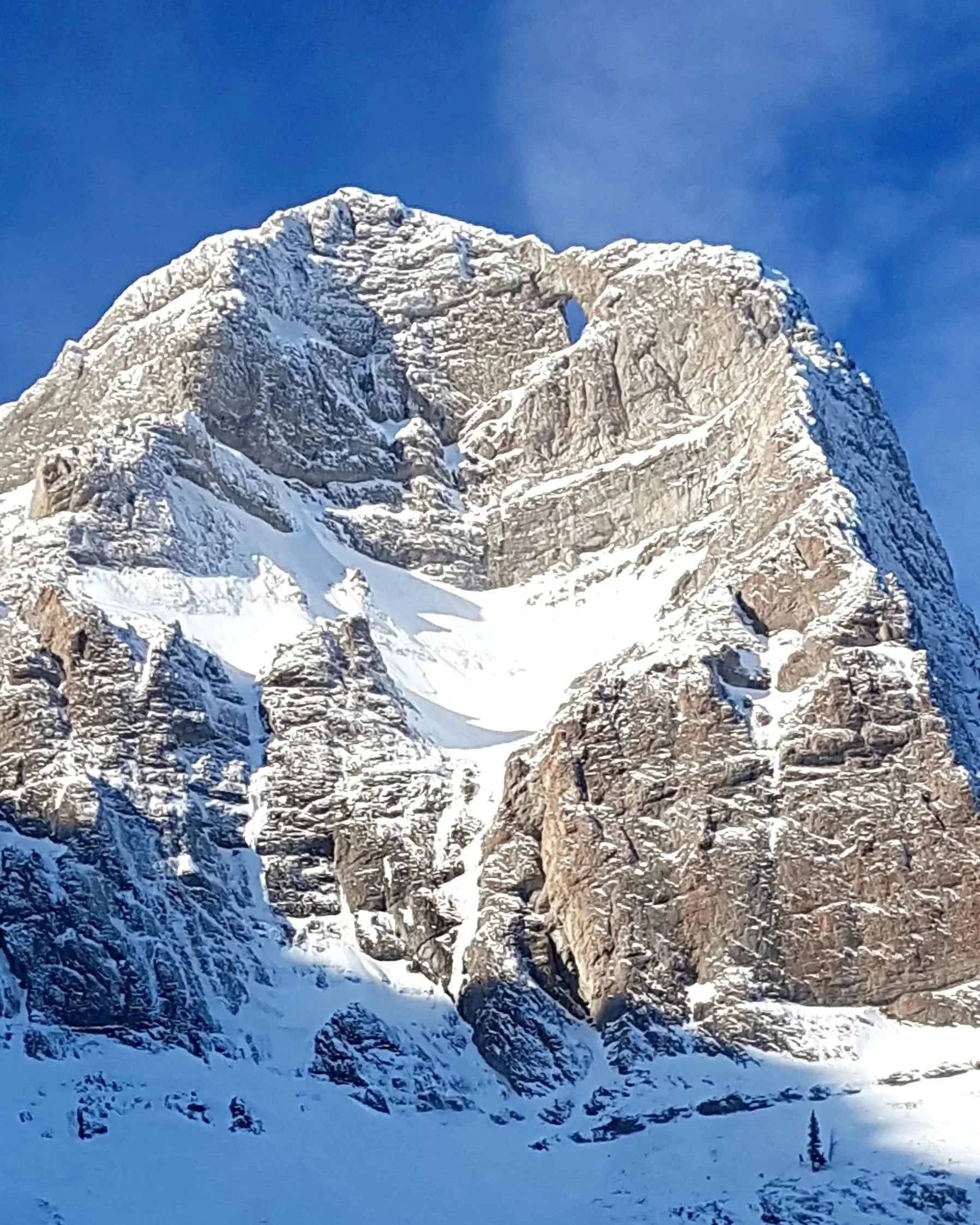 Snow-covered mountain with rocky slopes and a blue sky.