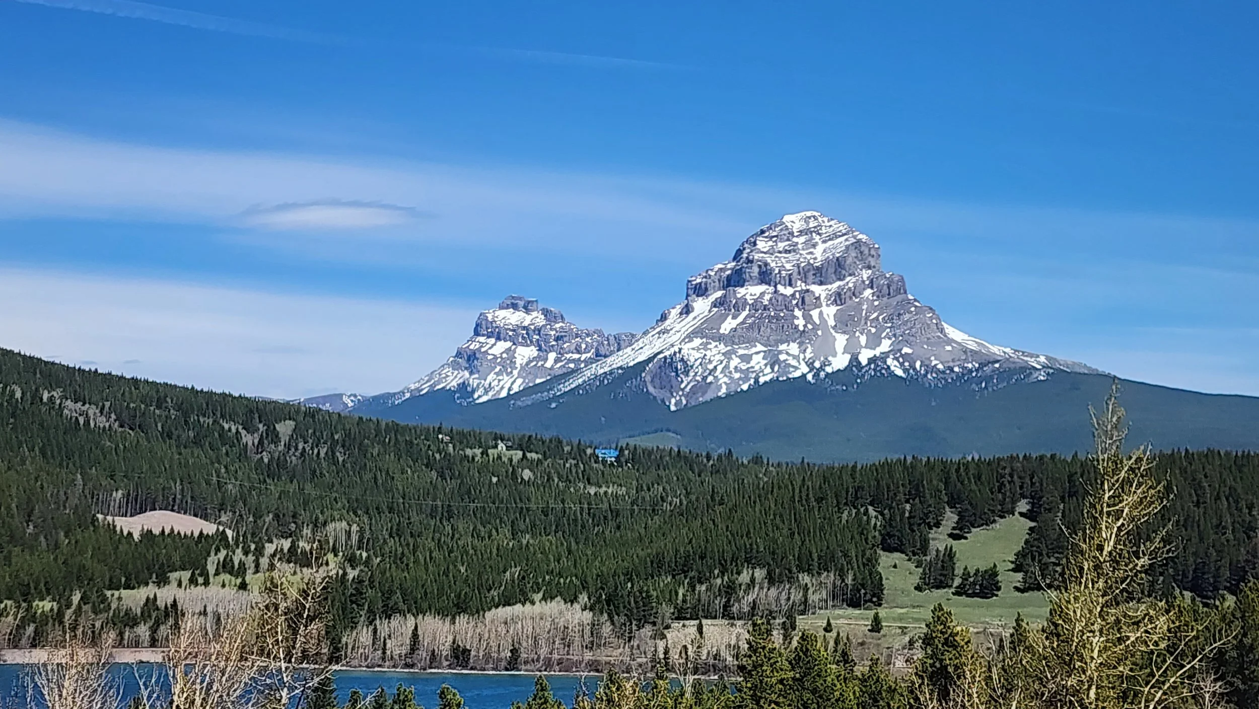 Scenic view of a snow-capped mountain with green forested hills in the foreground and a lake at the bottom.