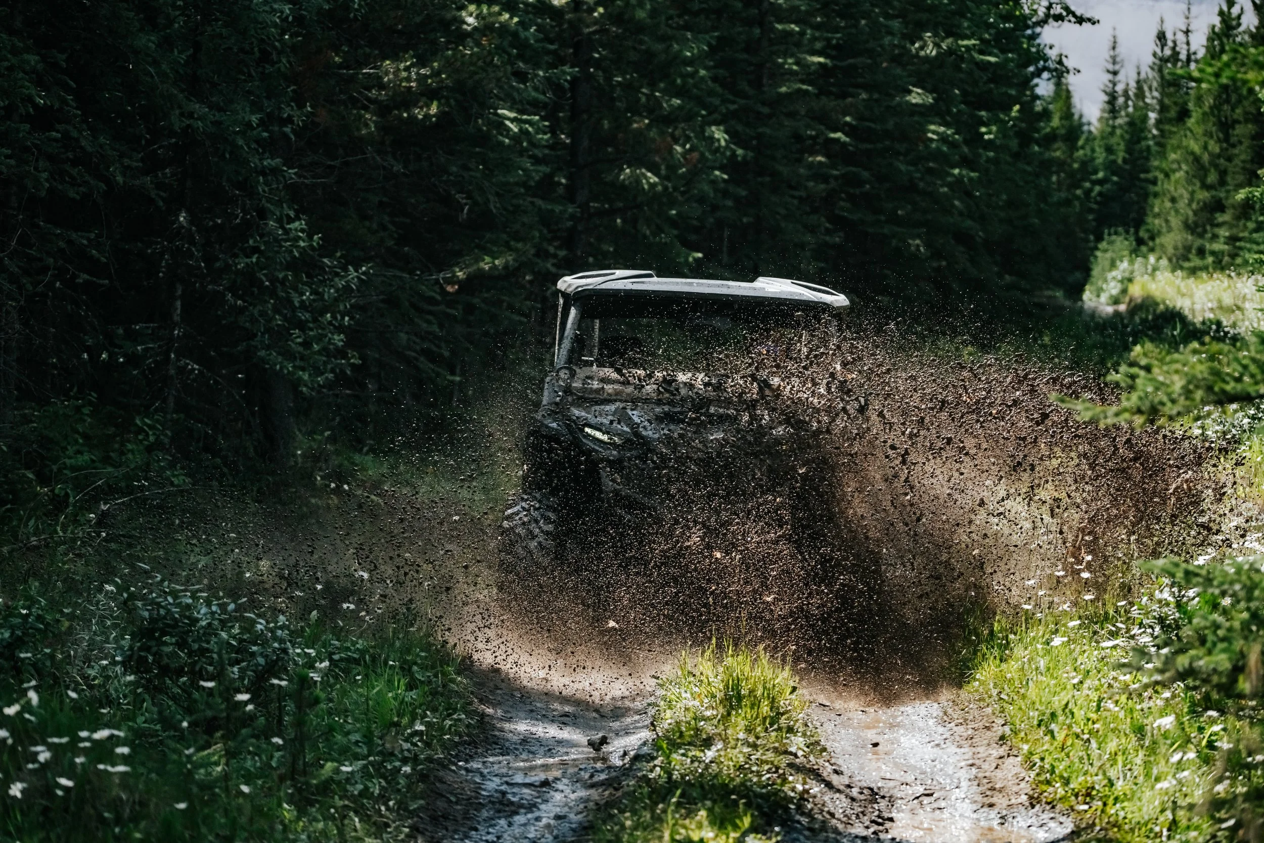 An all-terrain vehicle splashing through mud on a forest trail.