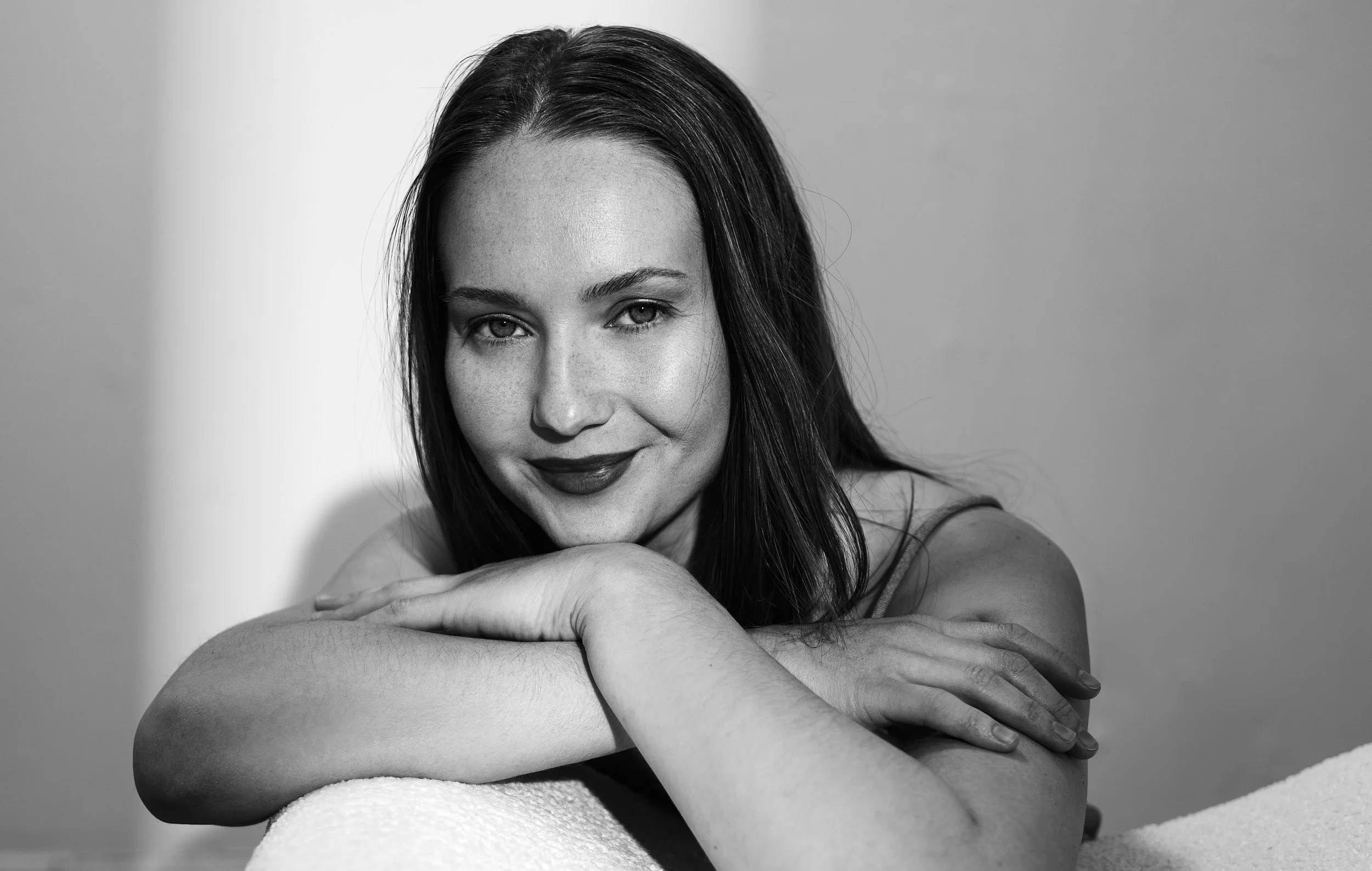 Black and white portrait of a woman with shoulder-length dark hair, resting her chin on her crossed arms, smiling softly at the camera.