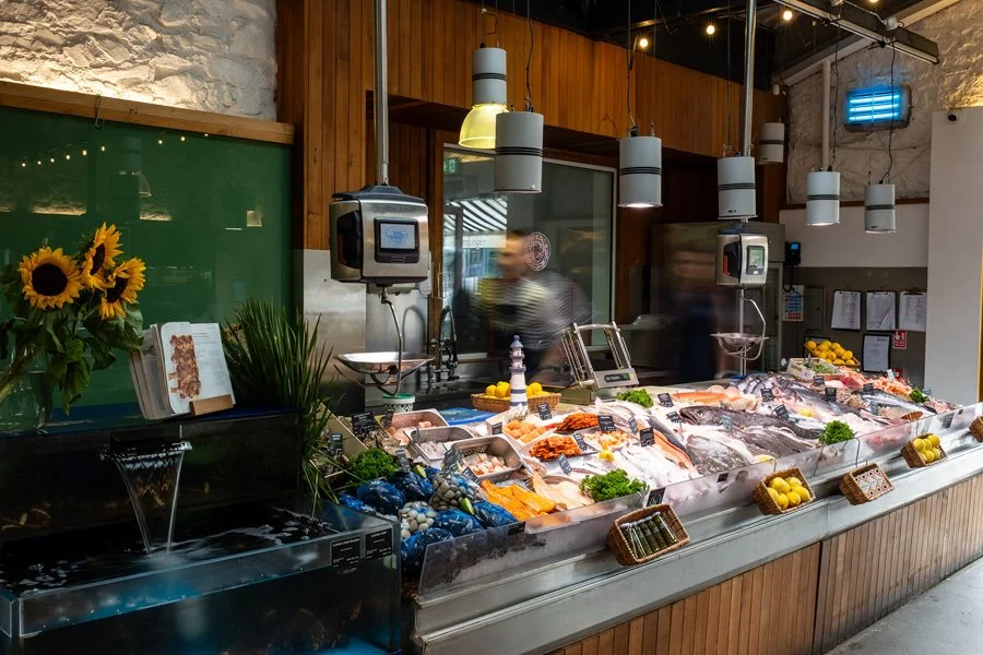 Seafood display counter with various fish and shellfish surrounded by lemons, greens, and decorative items in Beshoffs of Howth.