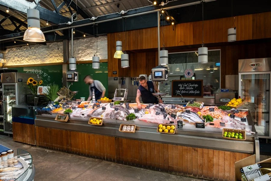 Indoor fish market display with fresh fish on ice, surrounded by lemons, and two workers in aprons preparing the seafood.