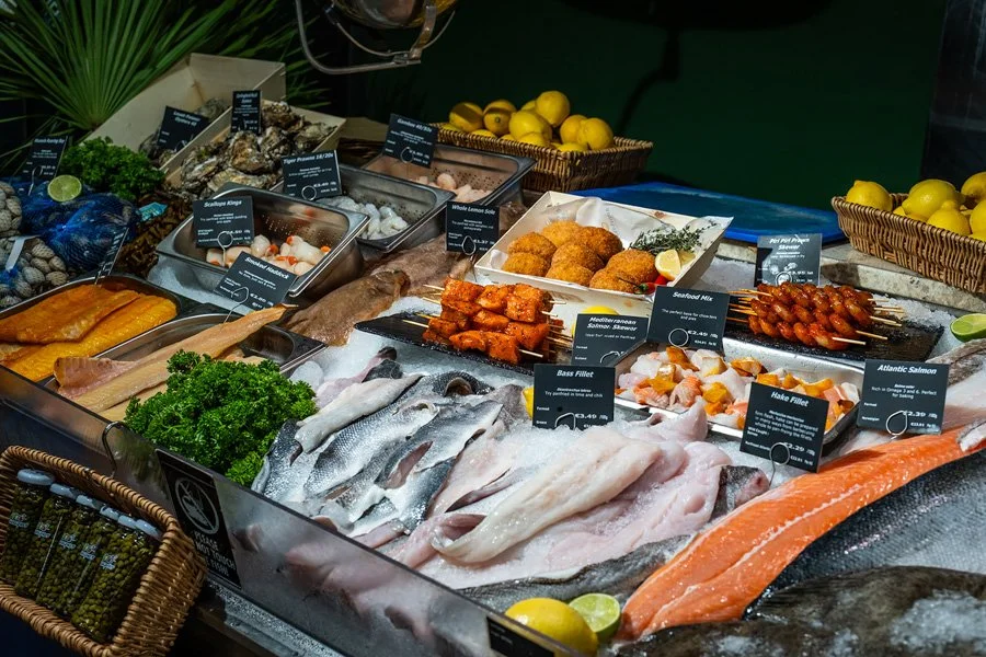 Fresh seafood display with fish fillets, skewered seafood, and oysters, along with lemons, greens, and various seafood labels displayed in the Beshoffs of Howth Market Hall.