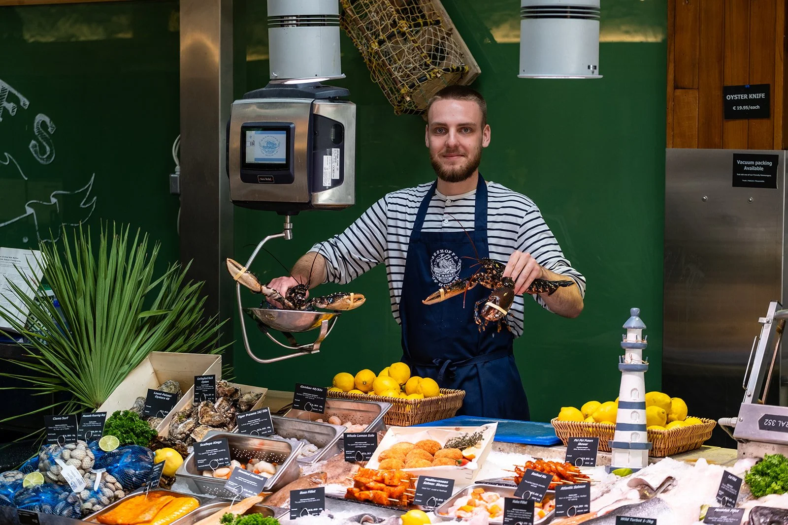 Man in striped shirt and apron holding lobsters behind a seafood display at Beshoffs of Howth Fishmongers.