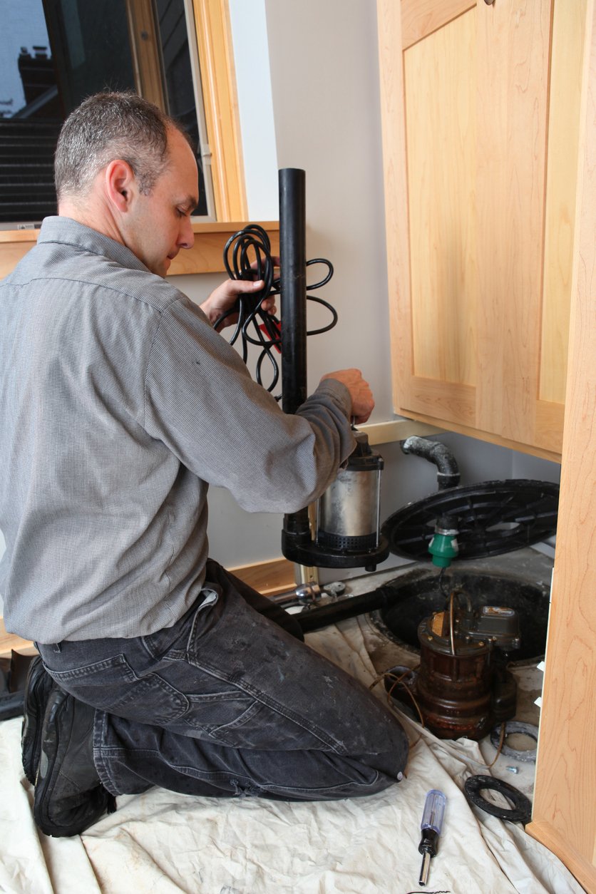 Man installing sump pump in basement.