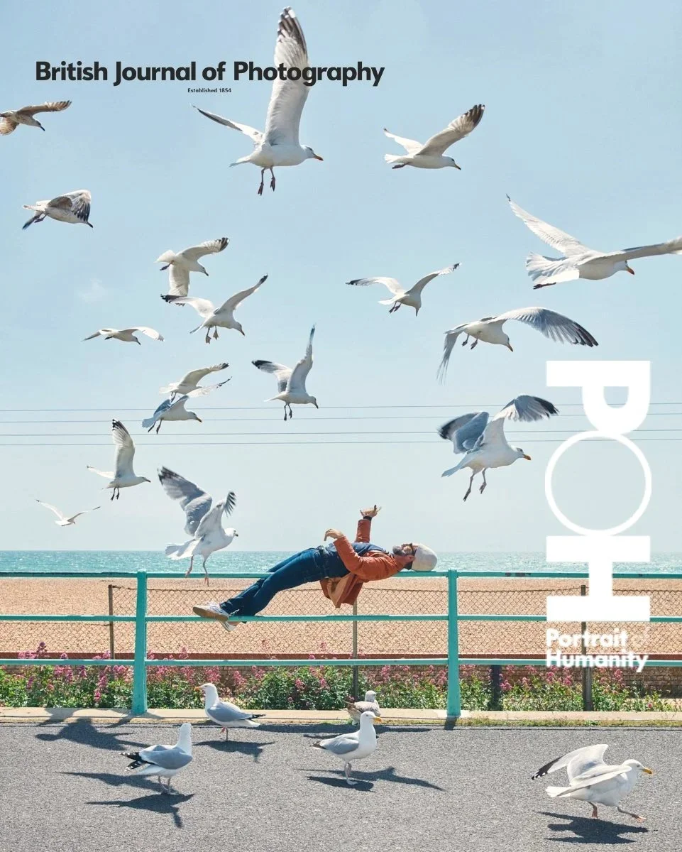 Cover of the British Journal of Photography featuring a person lying on a sidewalk near the beach, surrounded by seagulls flying and standing in the daylight.