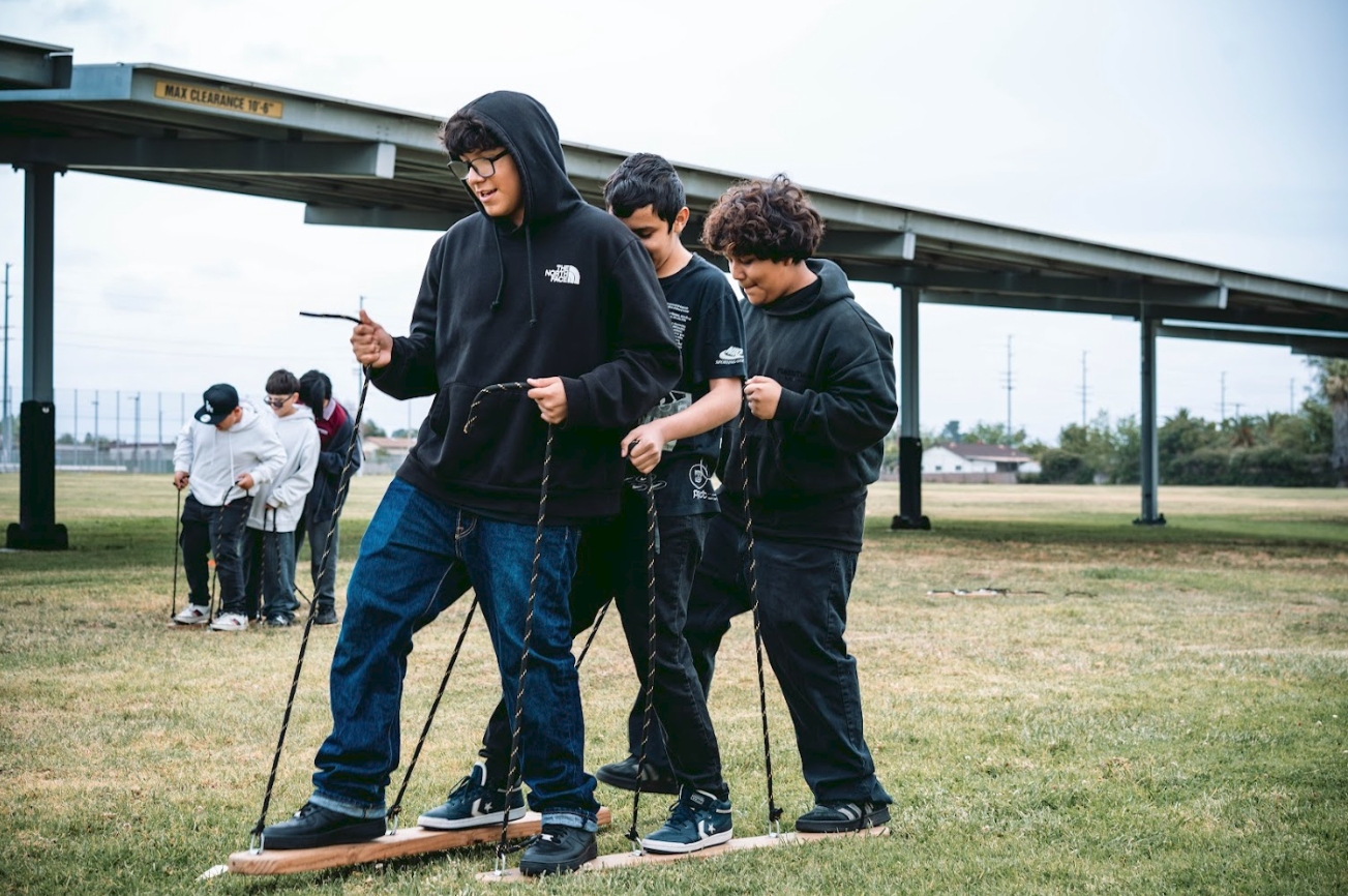 Group of children walking on wooden planks balanced with ropes during outdoor activity