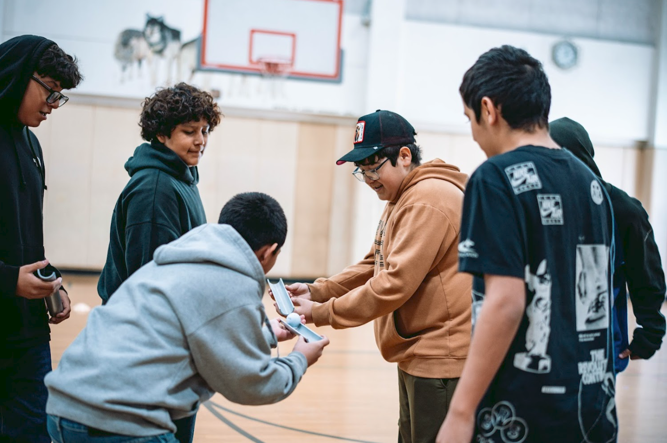 A group of children and a young adult in a gymnasium, with one of the children receiving an award or trophy from the young adult.