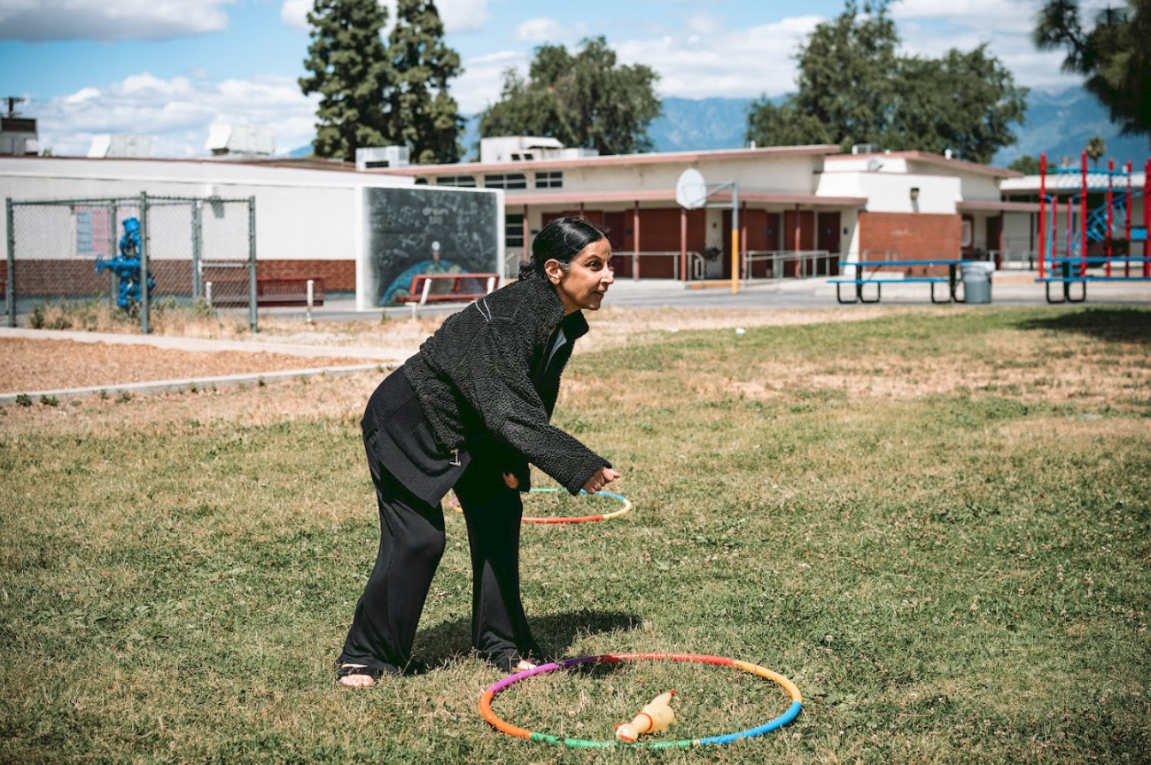 A woman playing with hula hoops on a schoolyard grassy field.
